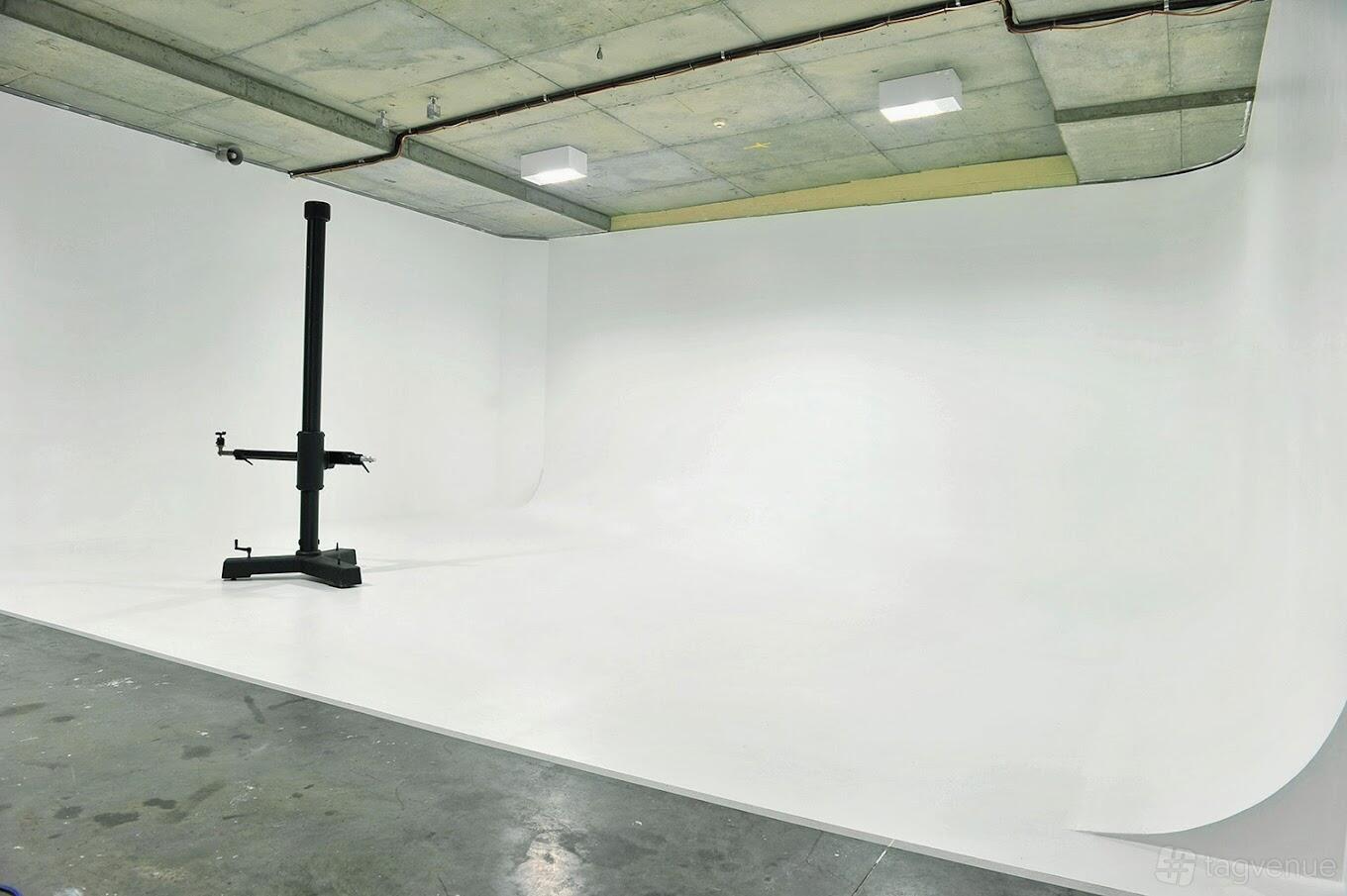 A photo studio with a large white cyclorama wall, concrete ceiling, and a camera stand at Smack Studios.