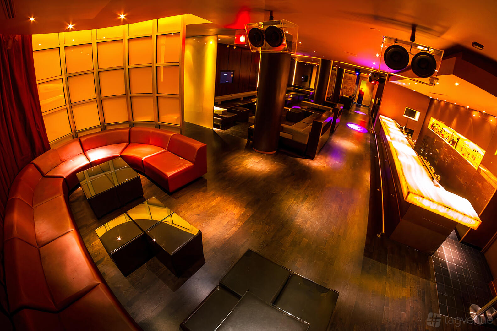 A bar with curved leather seating, dark wood floors, ambient lighting, and a long illuminated counter at Y Bar.