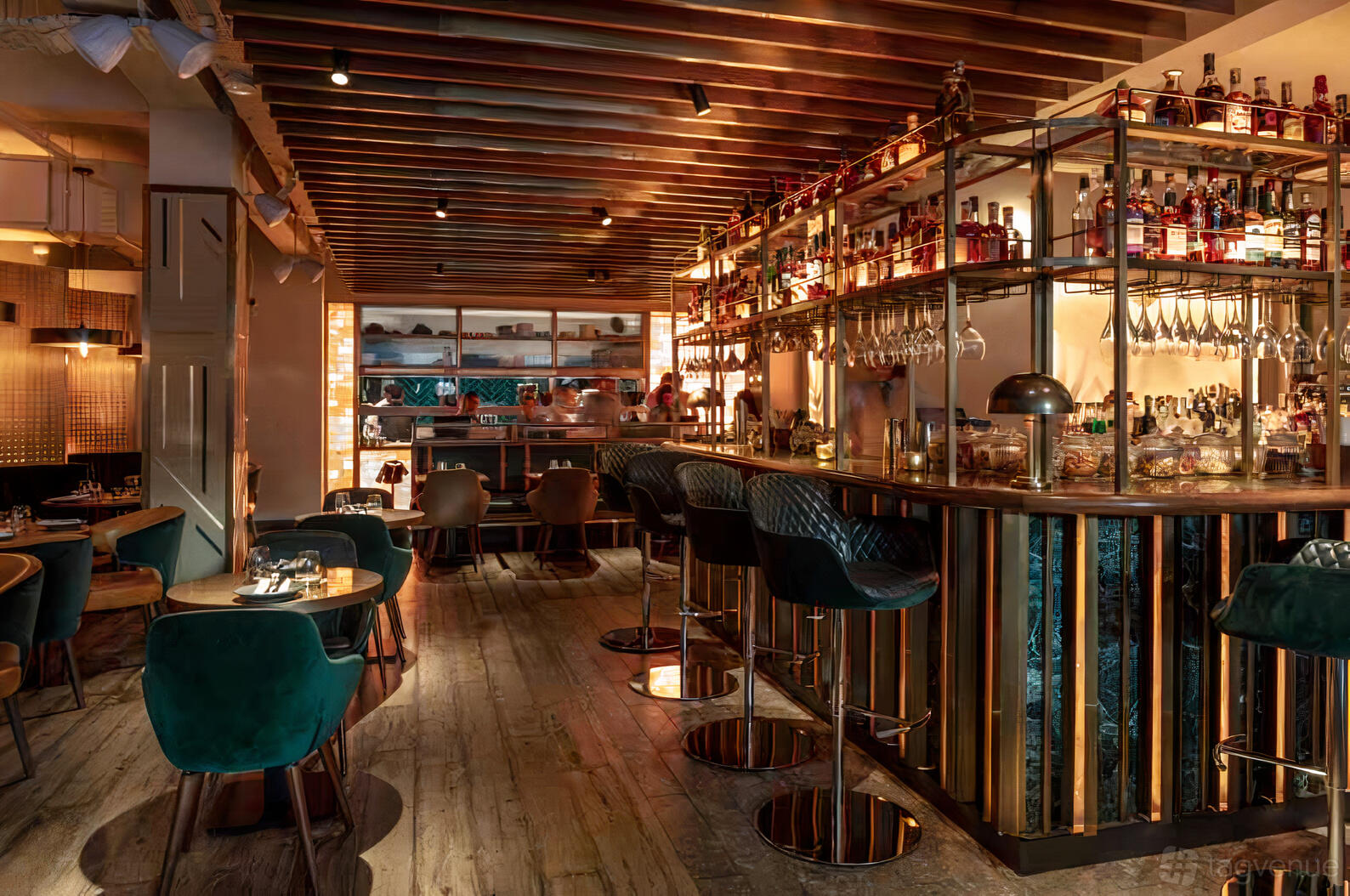 A restaurant with a long bar, high-backed velvet chairs, exposed wood ceiling, and shelves of bottles at Farzi London.