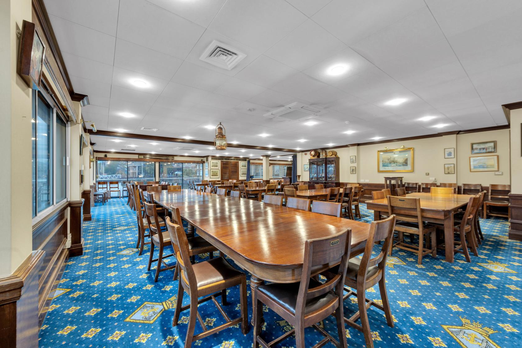 An event venue with long wooden tables, matching chairs, framed maritime artwork, and blue patterned carpet at Tower Hill, St. Katherine Docks.