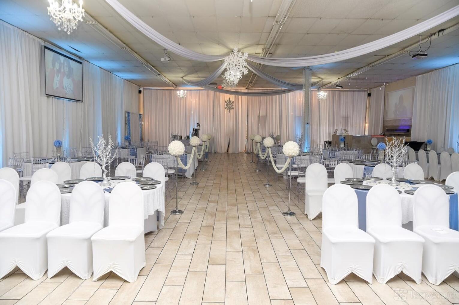 An event venue with draped white ceiling fabric, tiled floors, round tables with white chairs, and snowflake décor at Rendezvous Event Center.