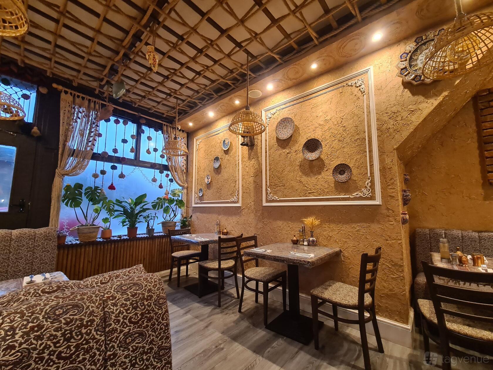 A restaurant with textured tan walls, hanging wicker lights, decorative wall plates, and patterned seating at Diyar Persian Grill House.