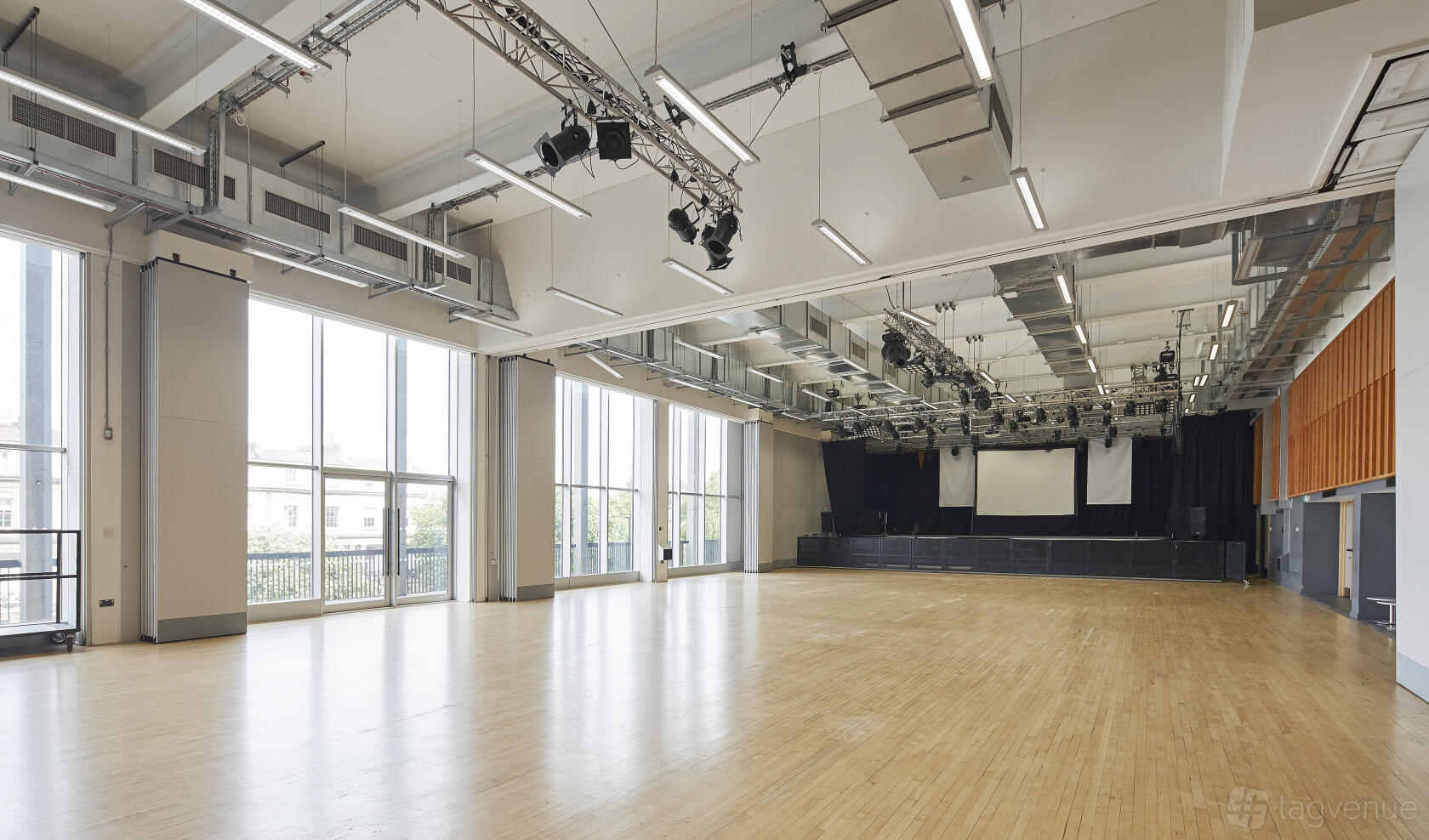 A spacious hall with a light wood floor, large windows, and stage with projection screens at University of Bristol Students' Union.