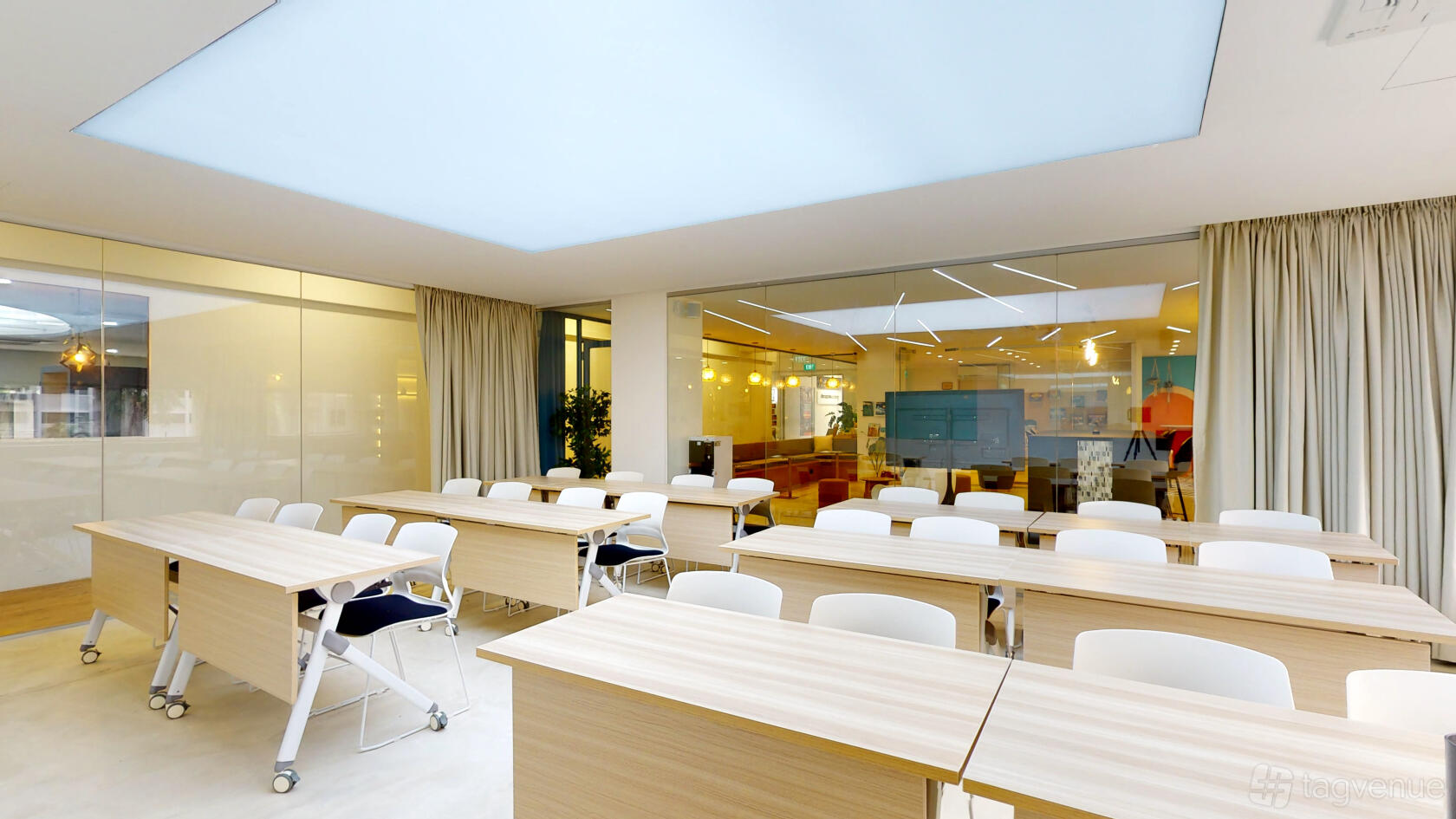 A meeting room with wood tables, white chairs, a glass wall, and a large skylight ceiling at Wings of the Dawn.