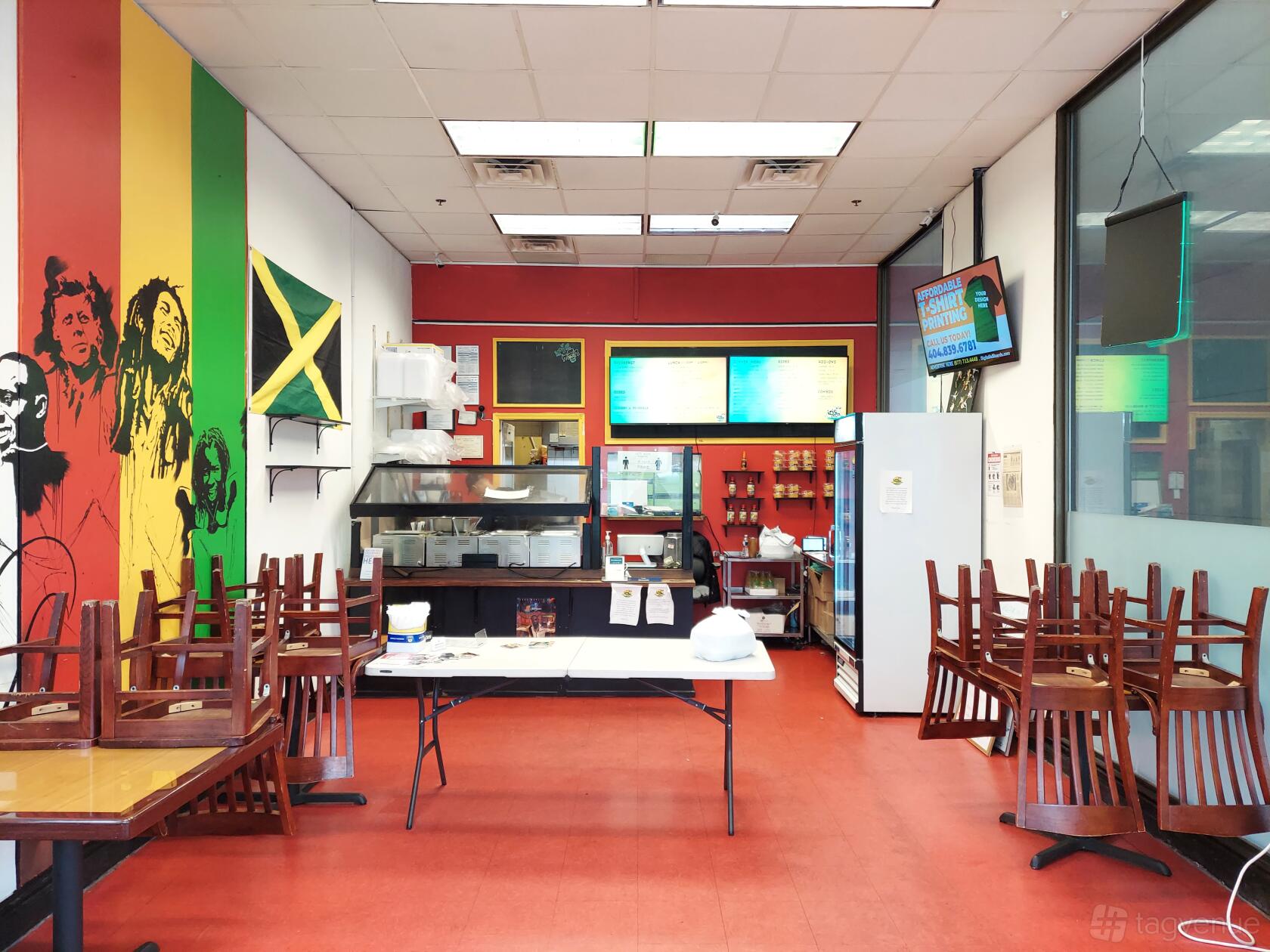 A restaurant with bold mural art, a Jamaican flag, red floors, and tables with chairs stacked at Irie Mon Cafe.