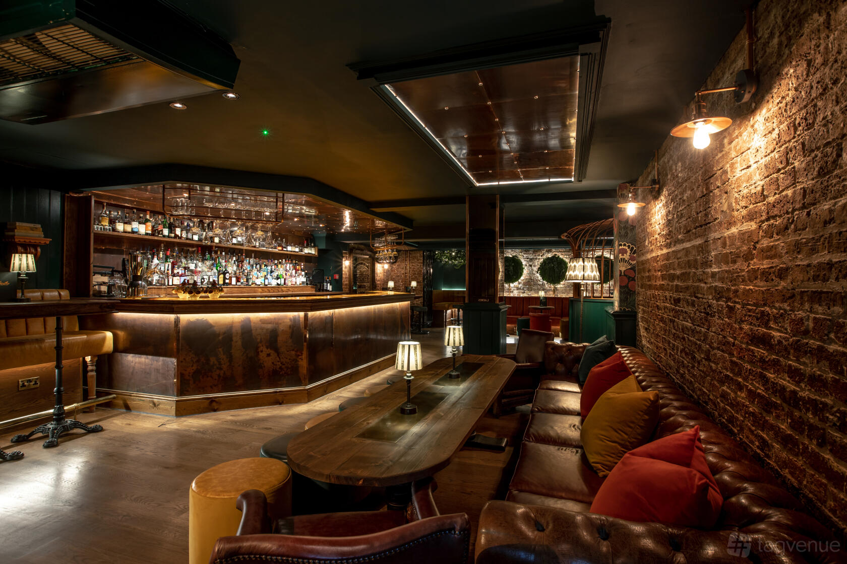 A cocktail bar with exposed brick walls, leather sofas, low wooden tables, and a backlit bar at Smiths Cocktail Bar.