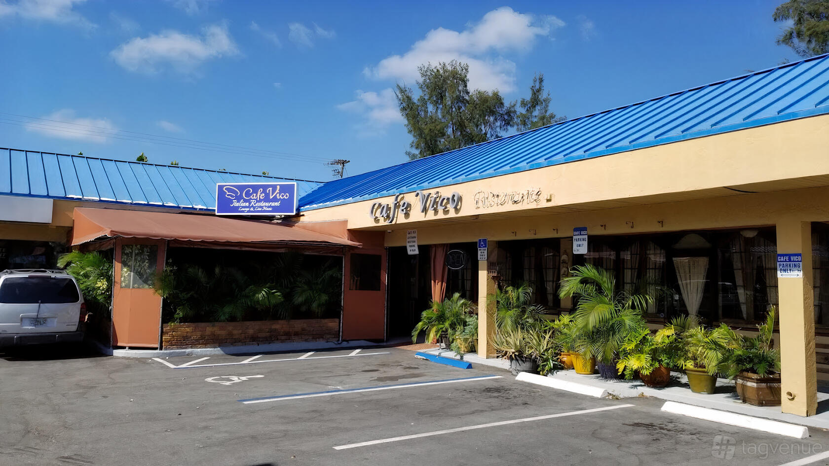 A restaurant with a blue metal roof, tan exterior walls, large windows, and potted plants at Cafe Vico.