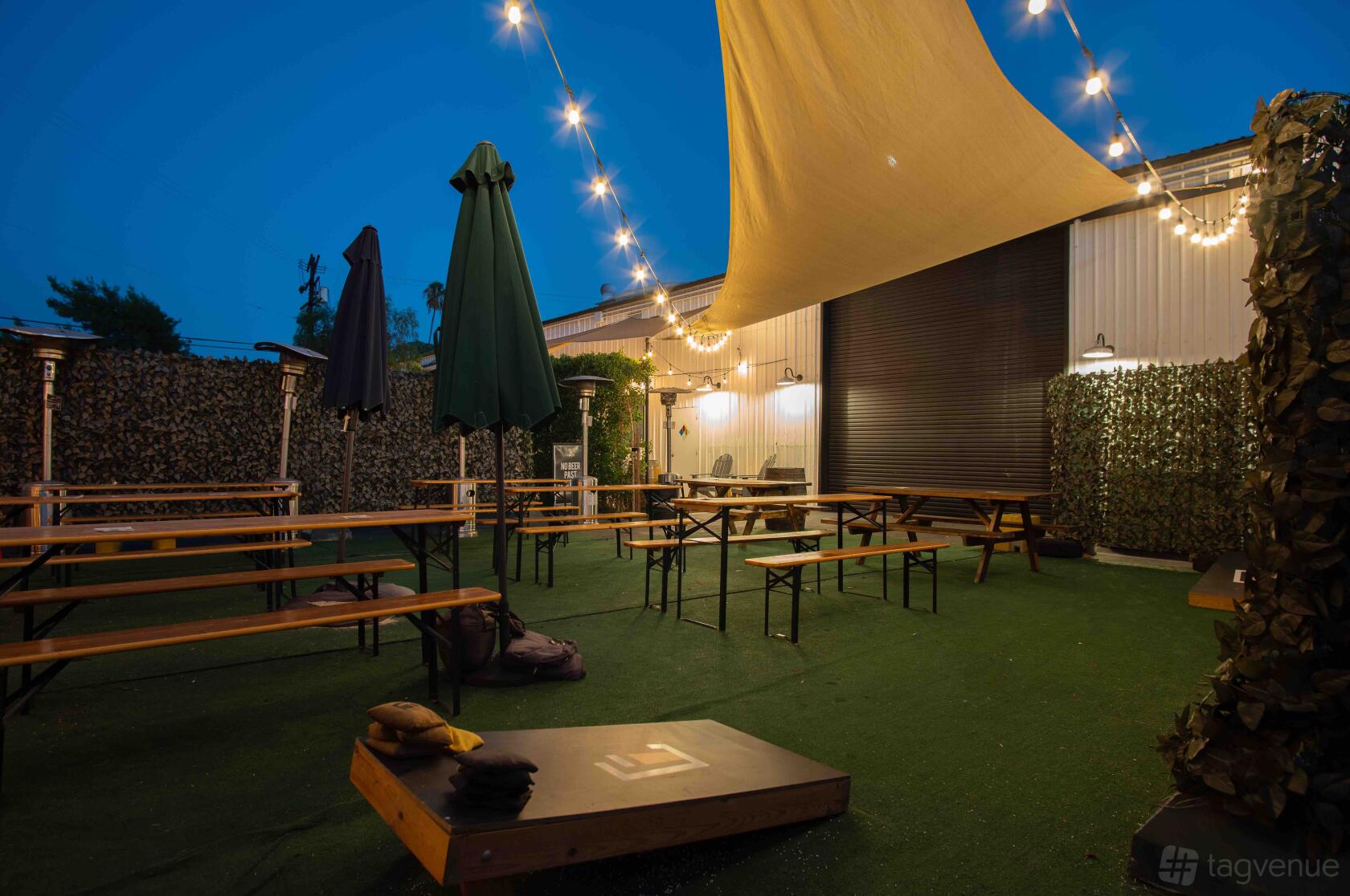 A terrace at a brewery with picnic benches, artificial turf, string lights, and sun shades at Lawless Brewing Co.