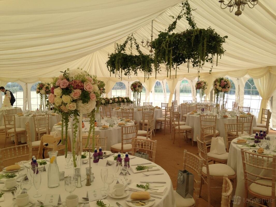 An event venue with a draped white marquee, round tables with white linens, and hanging greenery at Zinnia Gardens.