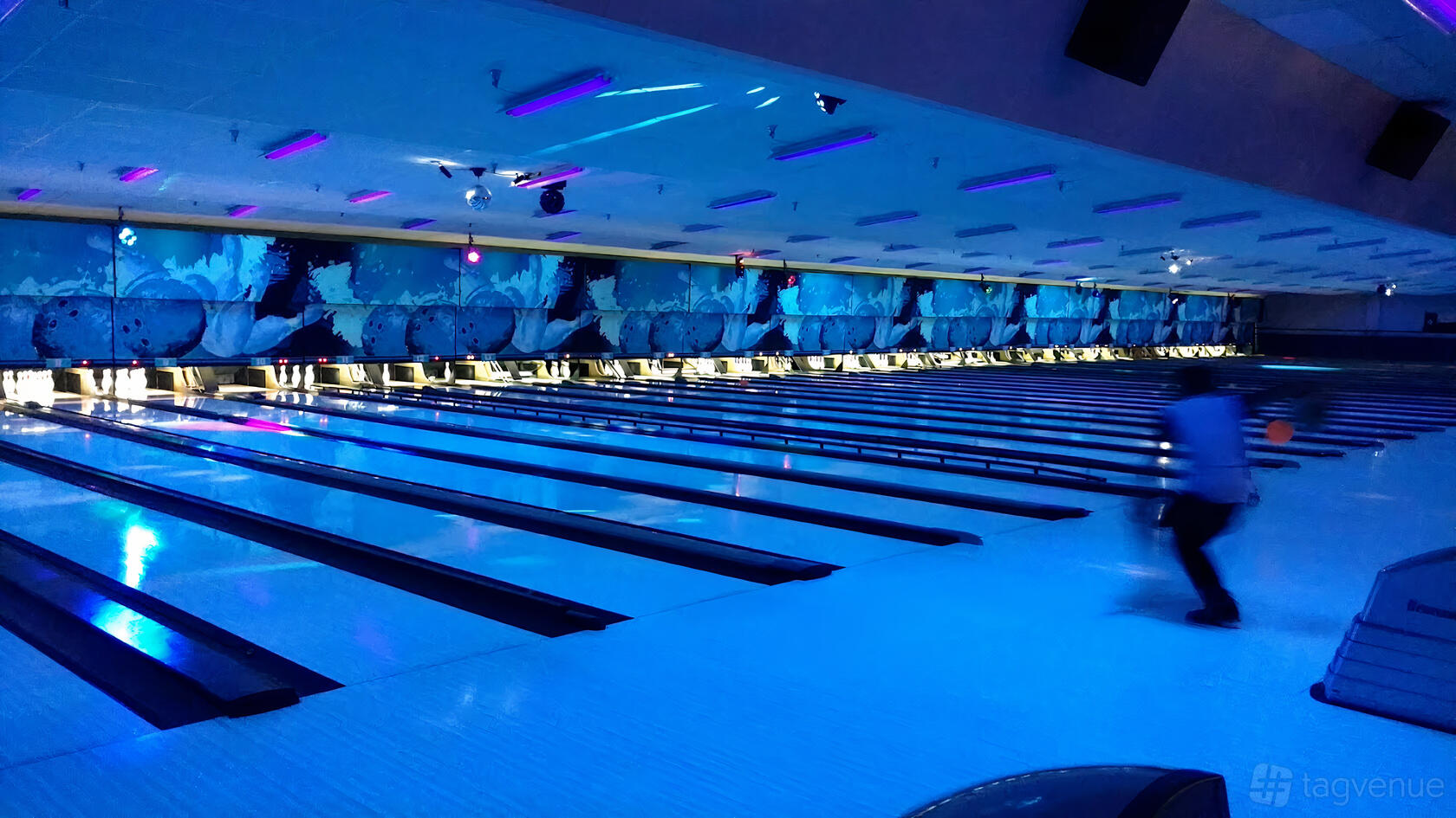 A bowling alley with neon-lit lanes, blue ambient lighting, and decorative wall murals at Westgate Lanes.