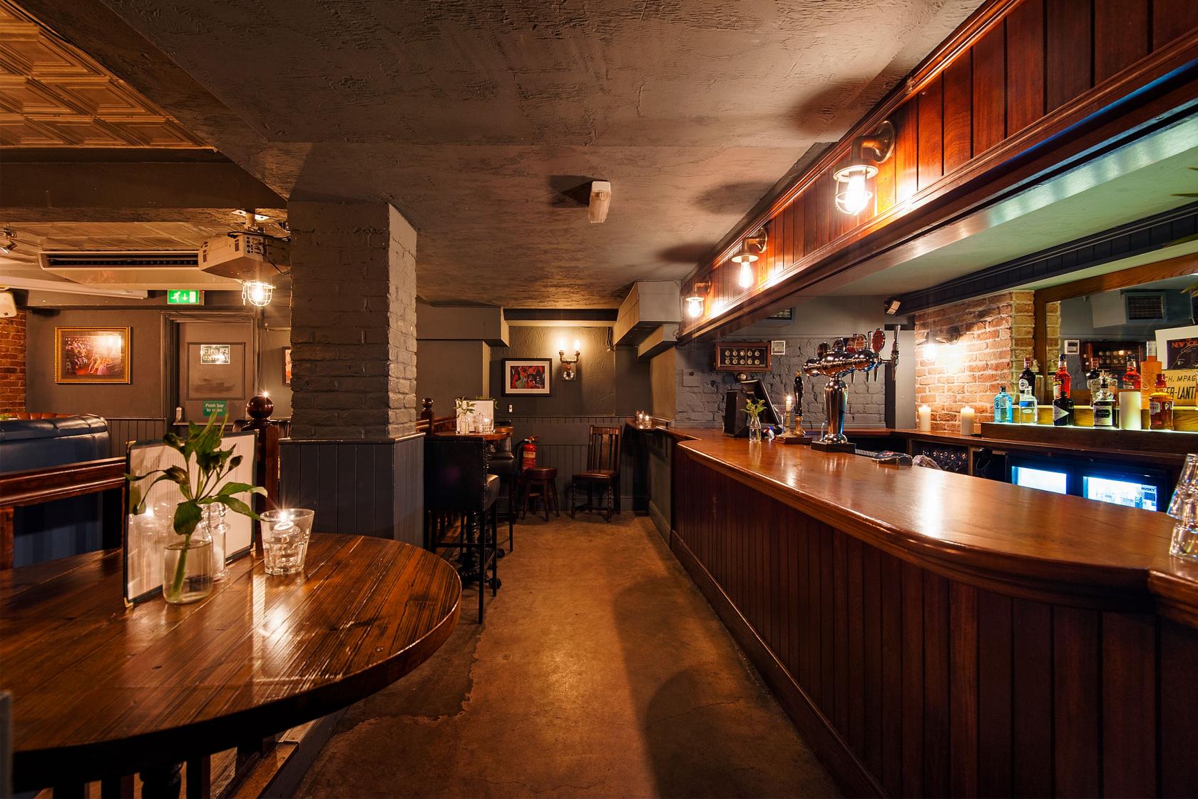An underground pub space with wood paneling, exposed brick, and a polished bar at The Washington.