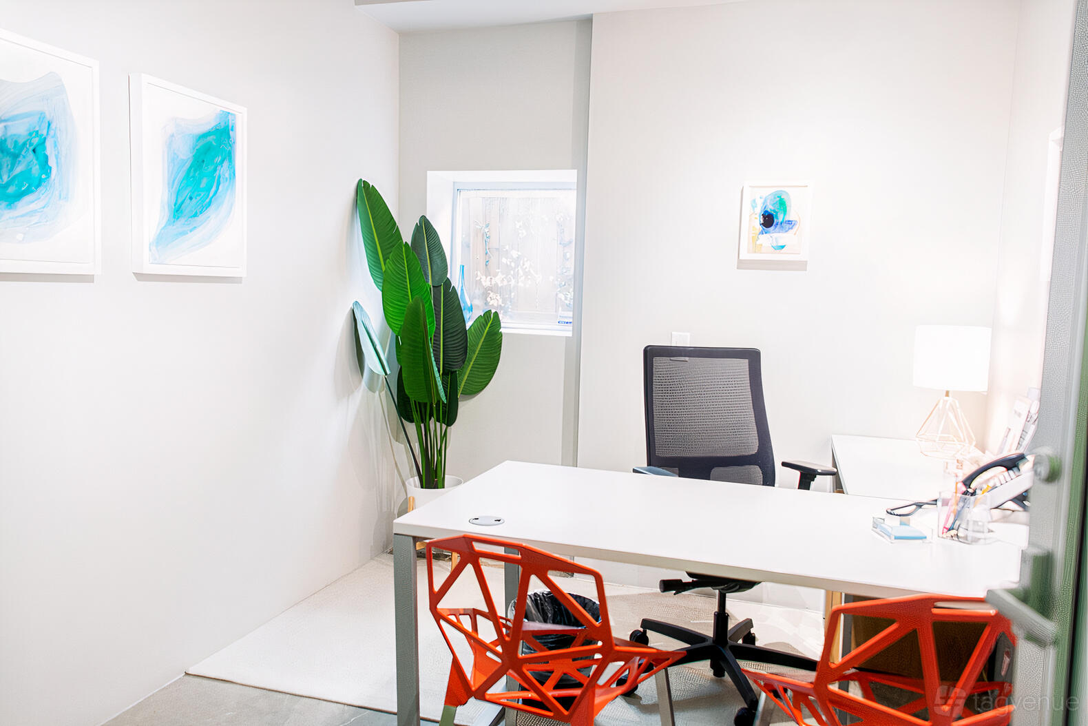 An office space with a large desk, orange chairs, potted plant, and abstract wall art at The Village Suites.