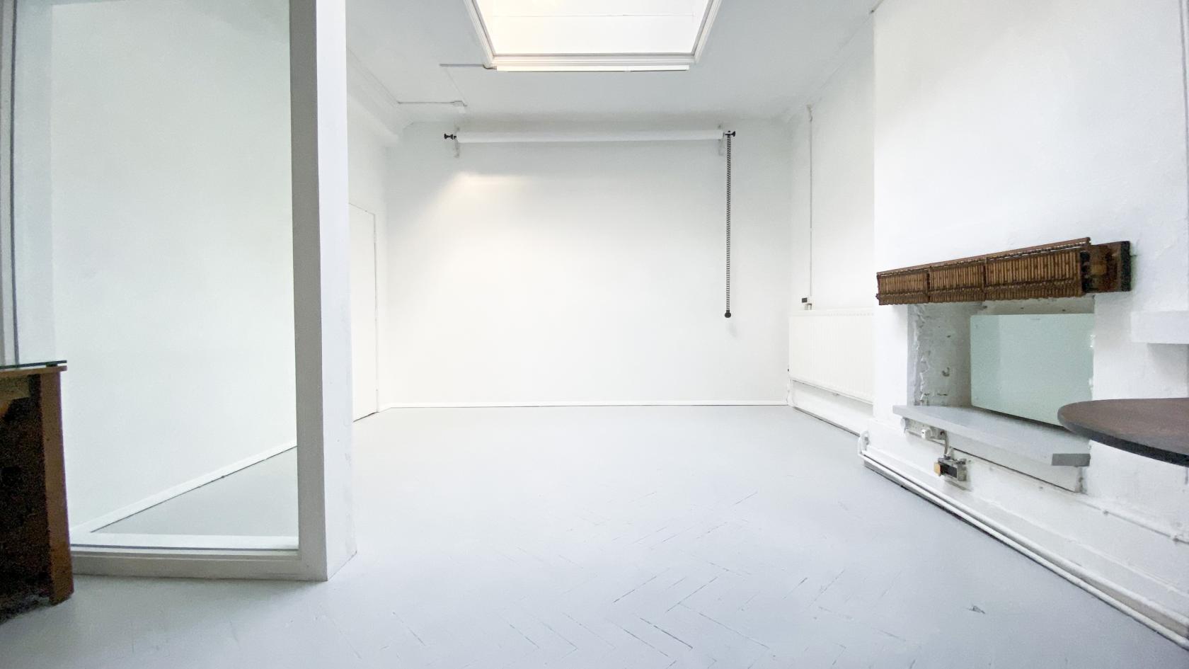 A photo studio with white walls, pale flooring, a large skylight, and a wall-mounted shelf at Butler in The Peanut Factory.