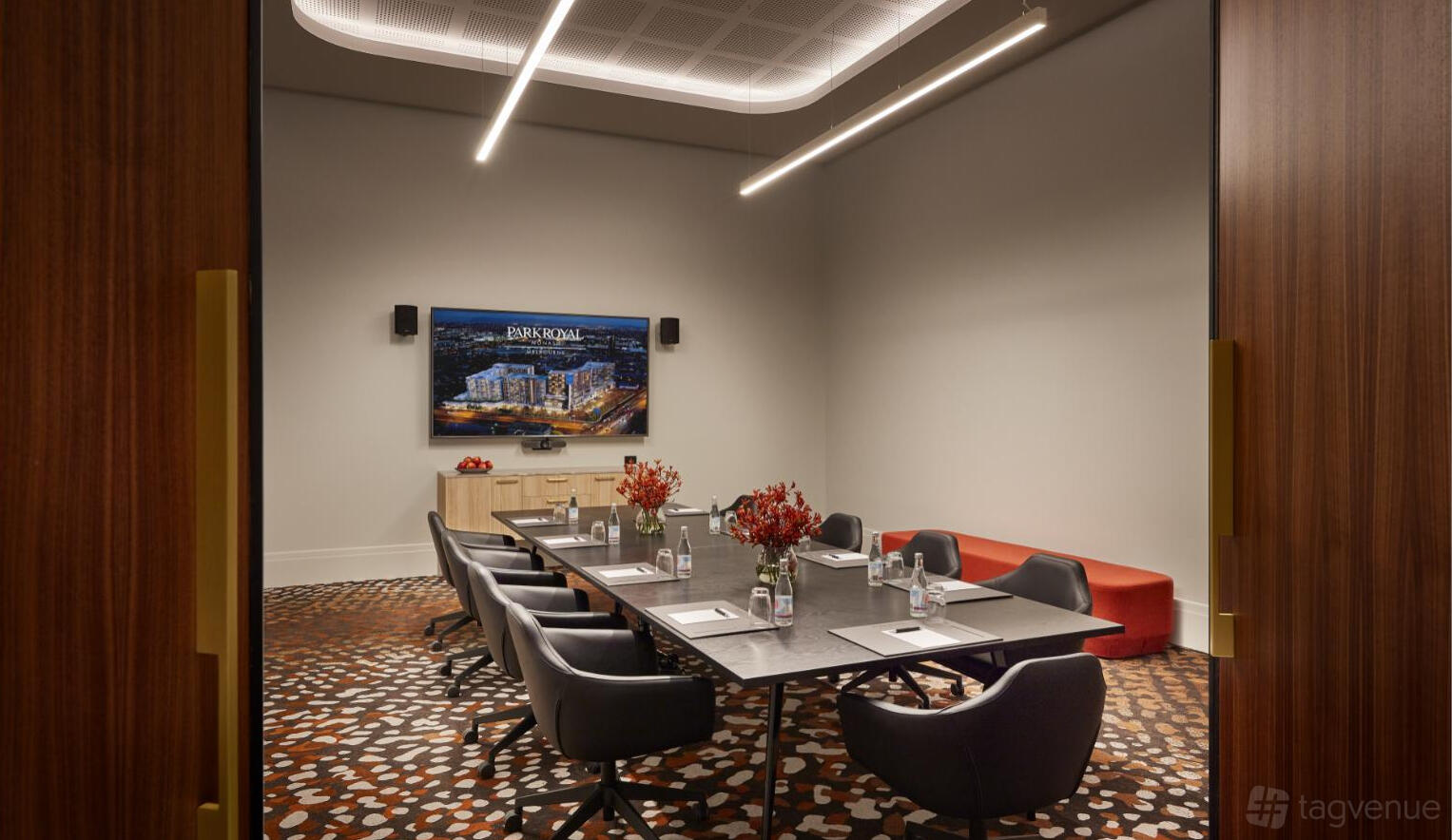 A hotel boardroom with a long meeting table, upholstered chairs, wall-mounted screen, and patterned carpet at PARKROYAL Monash Melbourne.