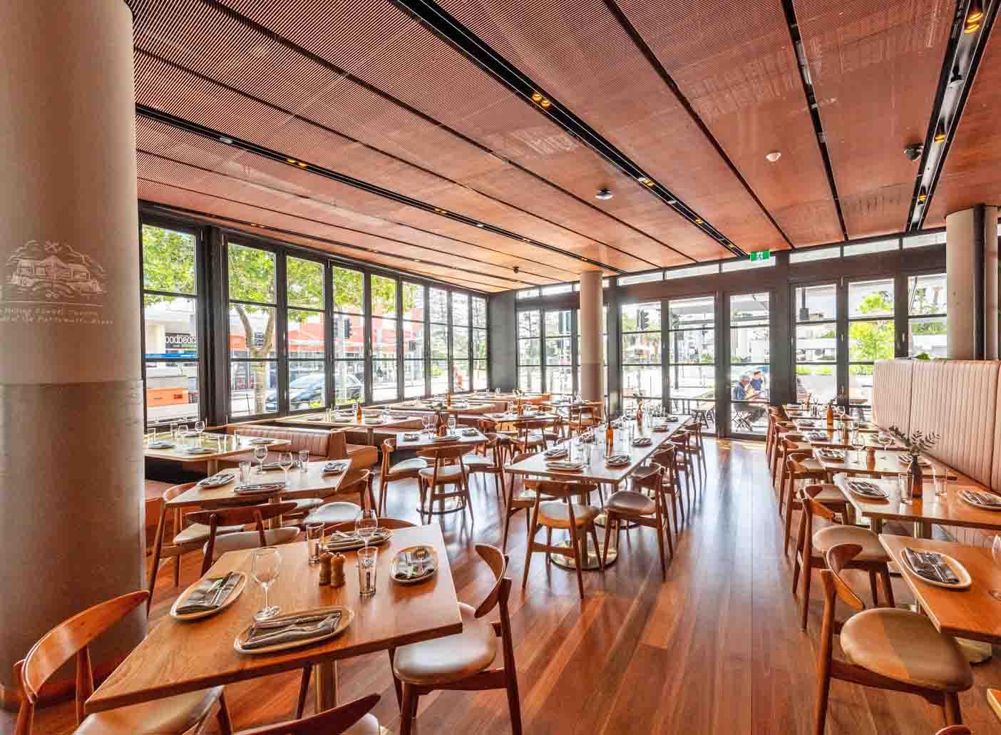 An event space in a bar with floor-to-ceiling windows, wooden tables, and natural lighting at The Lucky Squire.