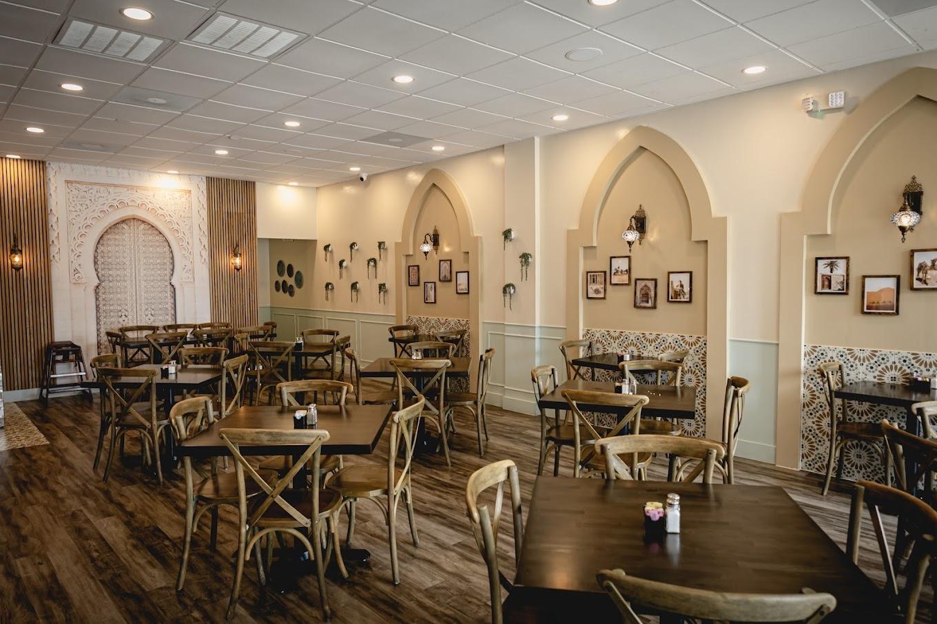 A restaurant with arched wall niches, framed photos, wooden tables, and patterned tile accents at Cafe Petra Greek & Lebanese - Missouri City.