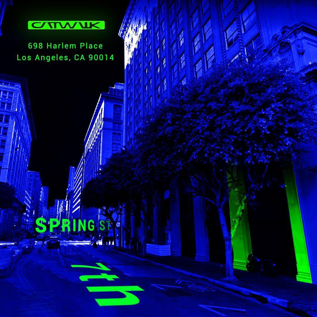A city street with tall buildings and trees illuminated by blue and green lighting near Catwalk.