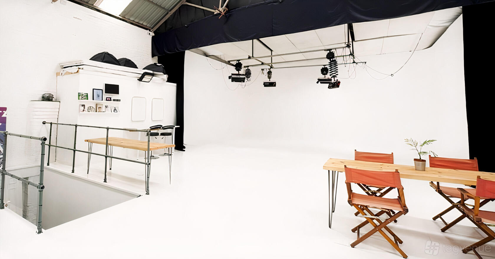 A photo studio with a large white cyclorama wall, overhead lighting rigs, and folding wooden chairs at Liverpool Studios.