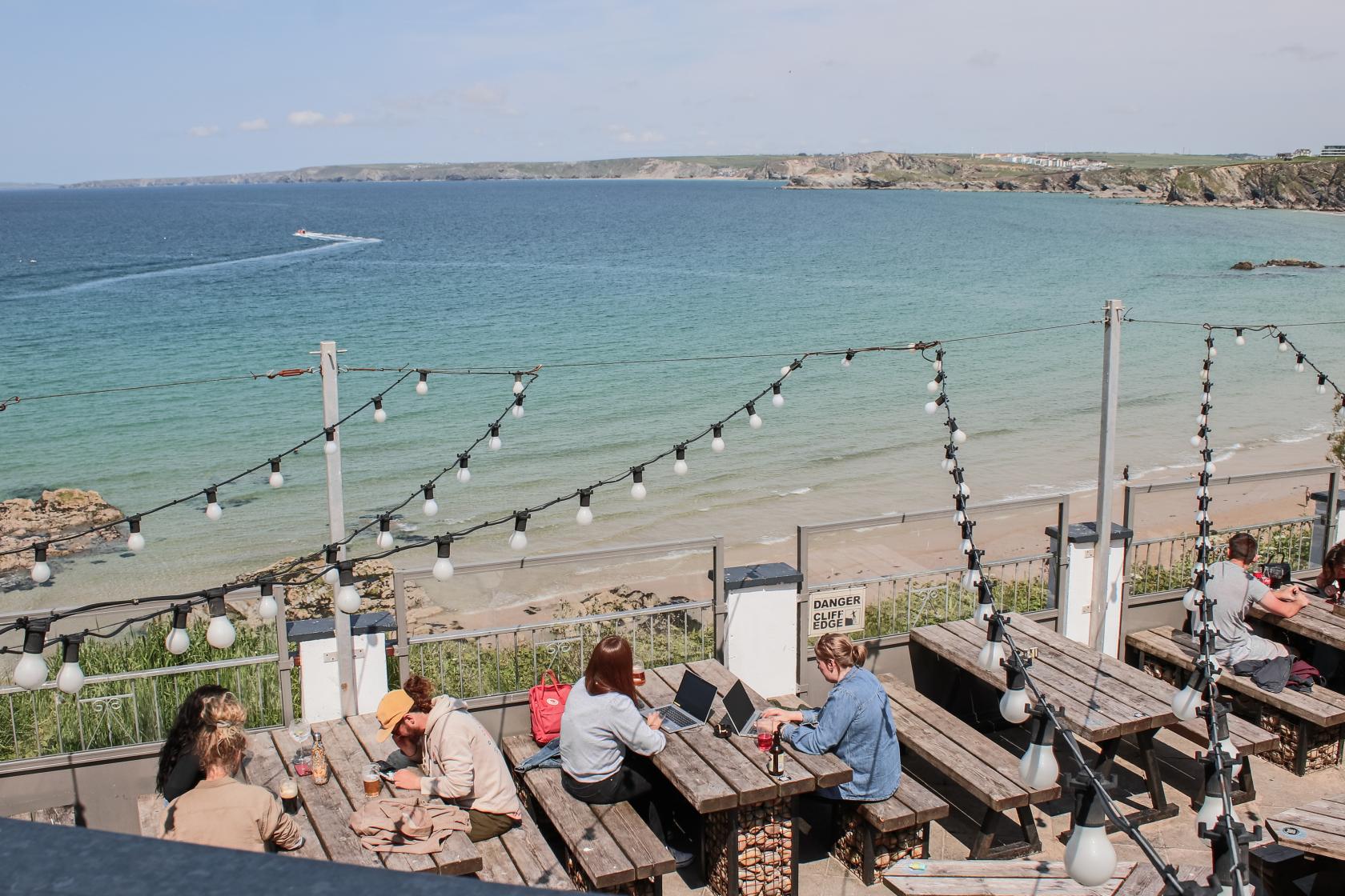 An outdoor event space with wooden benches, string lights, and beach views at Belushi's Newquay.