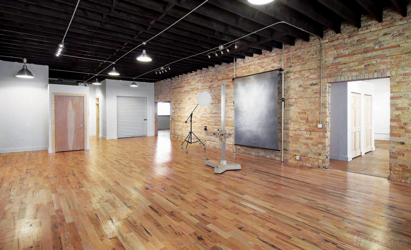 A photo studio with exposed brick walls, hardwood floors, studio lighting, and a backdrop at Throop Studio.