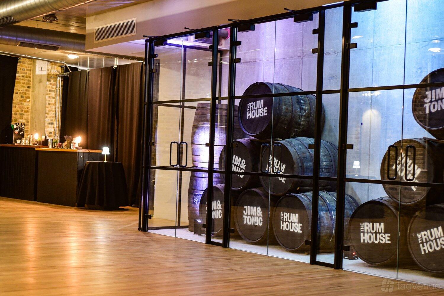 A function room with stacked rum barrels behind glass walls and exposed brick at The Rum House at Jim & Tonic East.