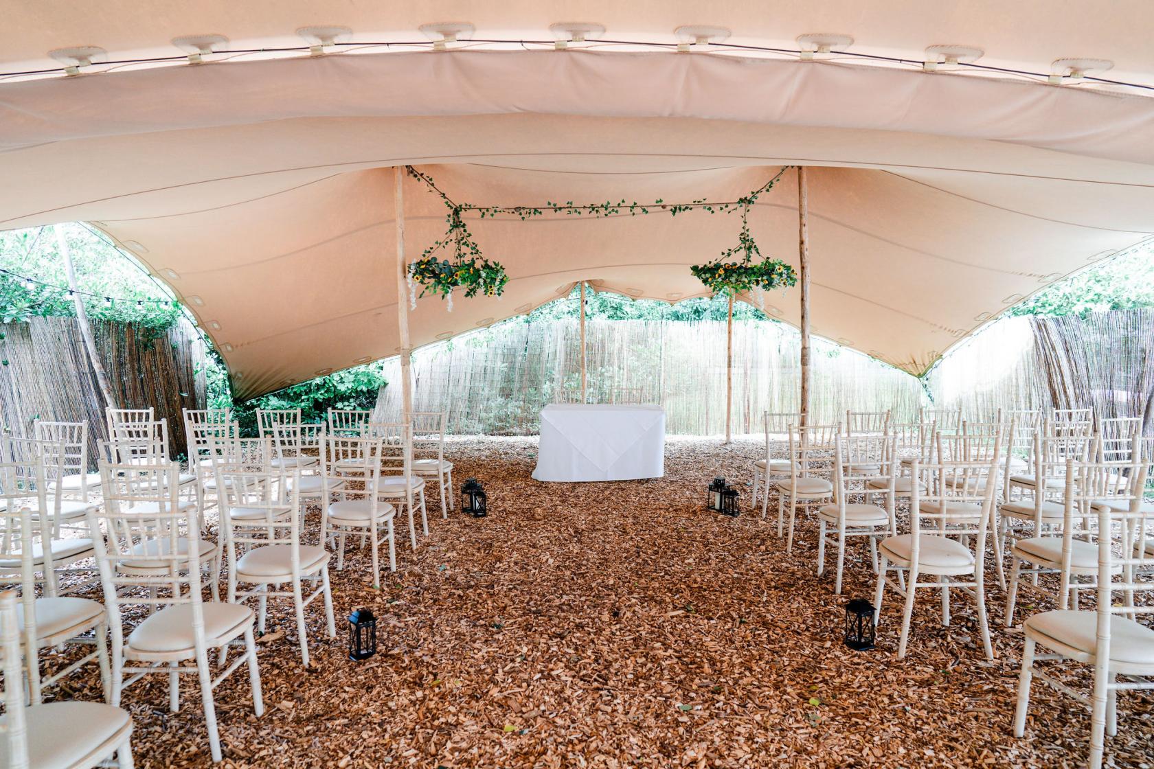 An event venue with a stretch tent, white chairs, woodchip floor, and hanging greenery at Old Rectory House.