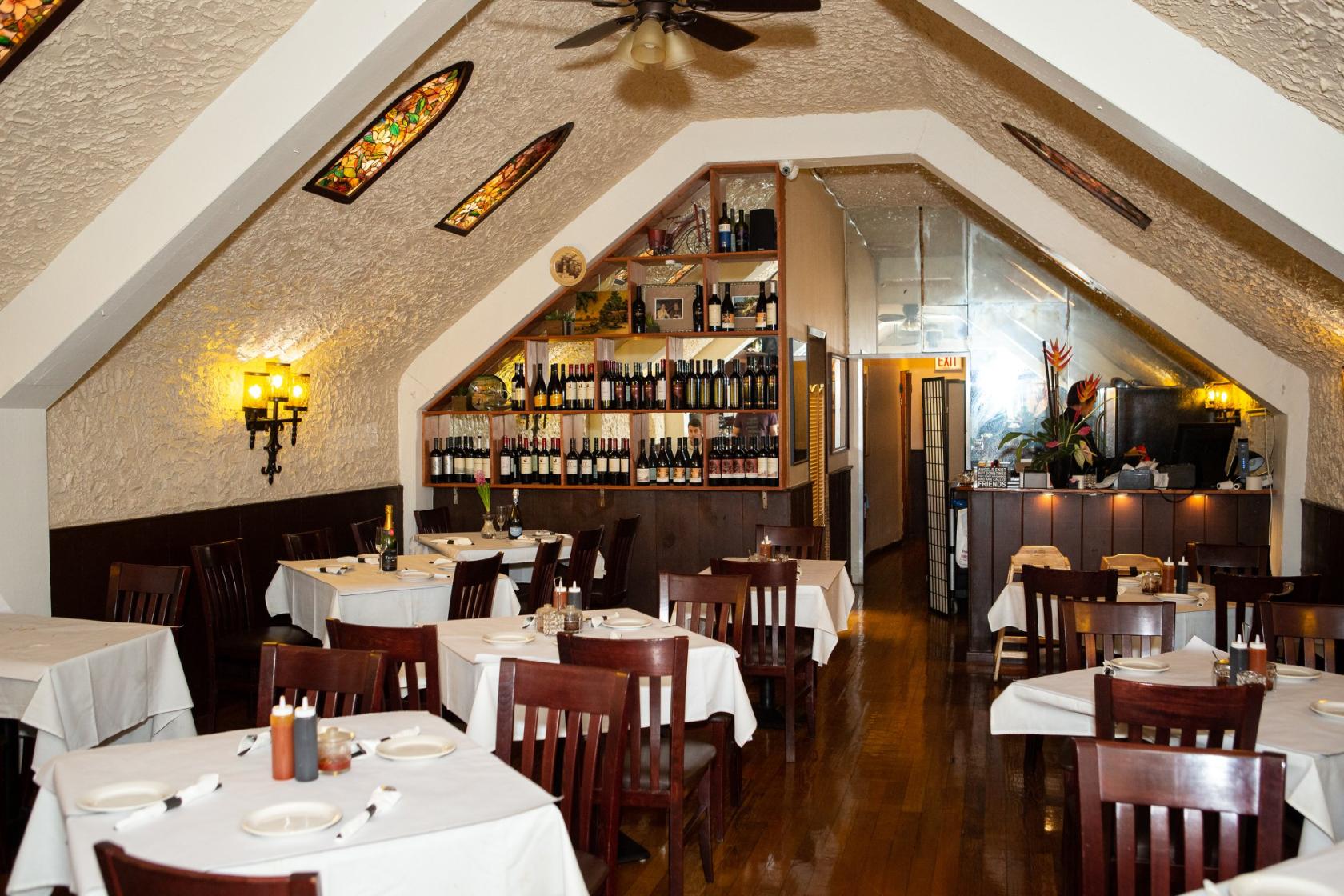 A restaurant with wooden chairs, white tablecloths, stained glass accents, and a wine display at Sunset Pho Caffe.