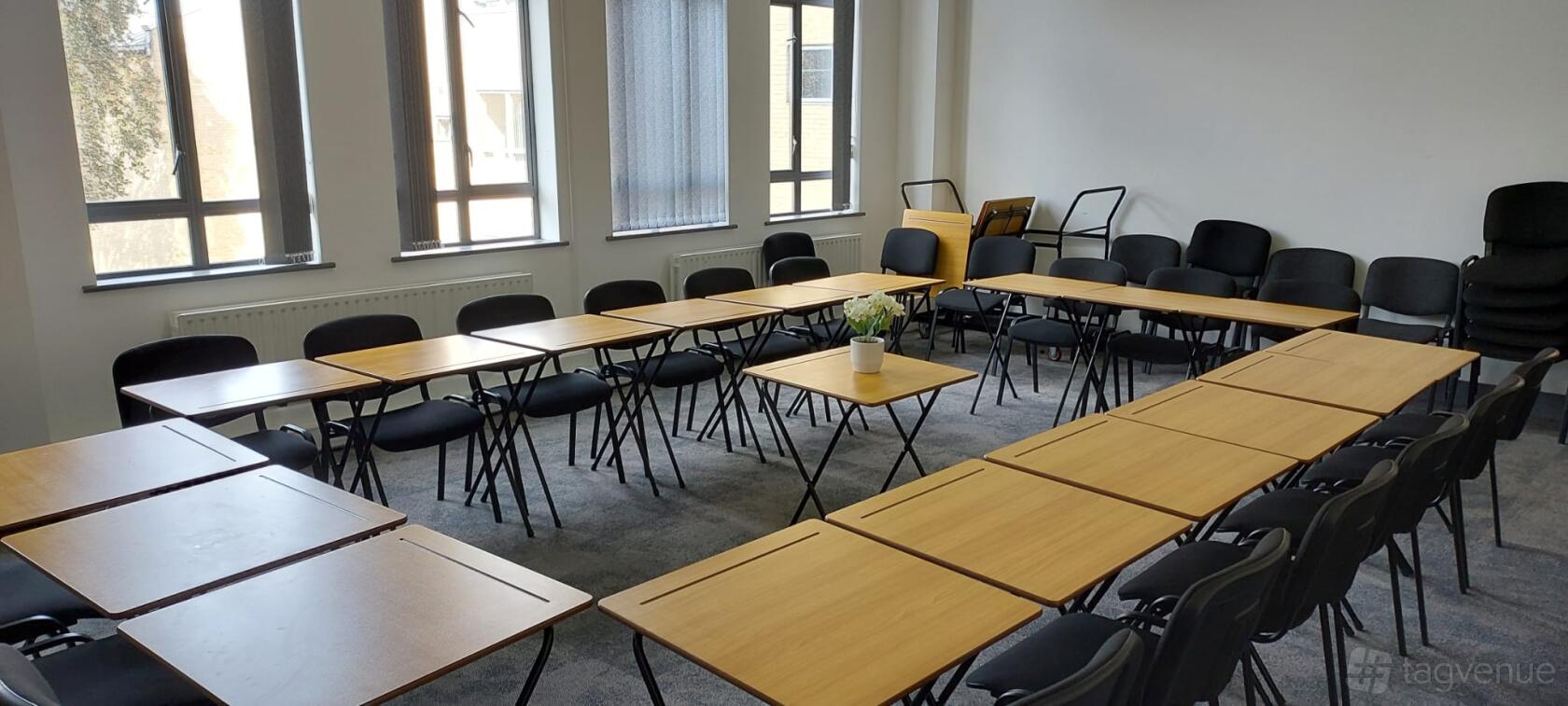 A meeting room with U-shaped arrangement of wooden tables, black chairs, and large windows at Rhythmic Skills.