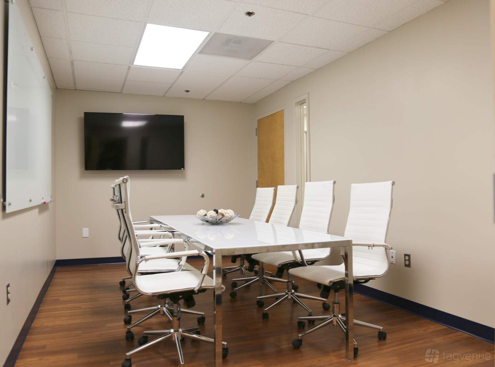 A meeting centre room with a glass-topped table, white leather chairs, wall-mounted TV, and a large whiteboard at Perfect Office Solutions - Beltsville.