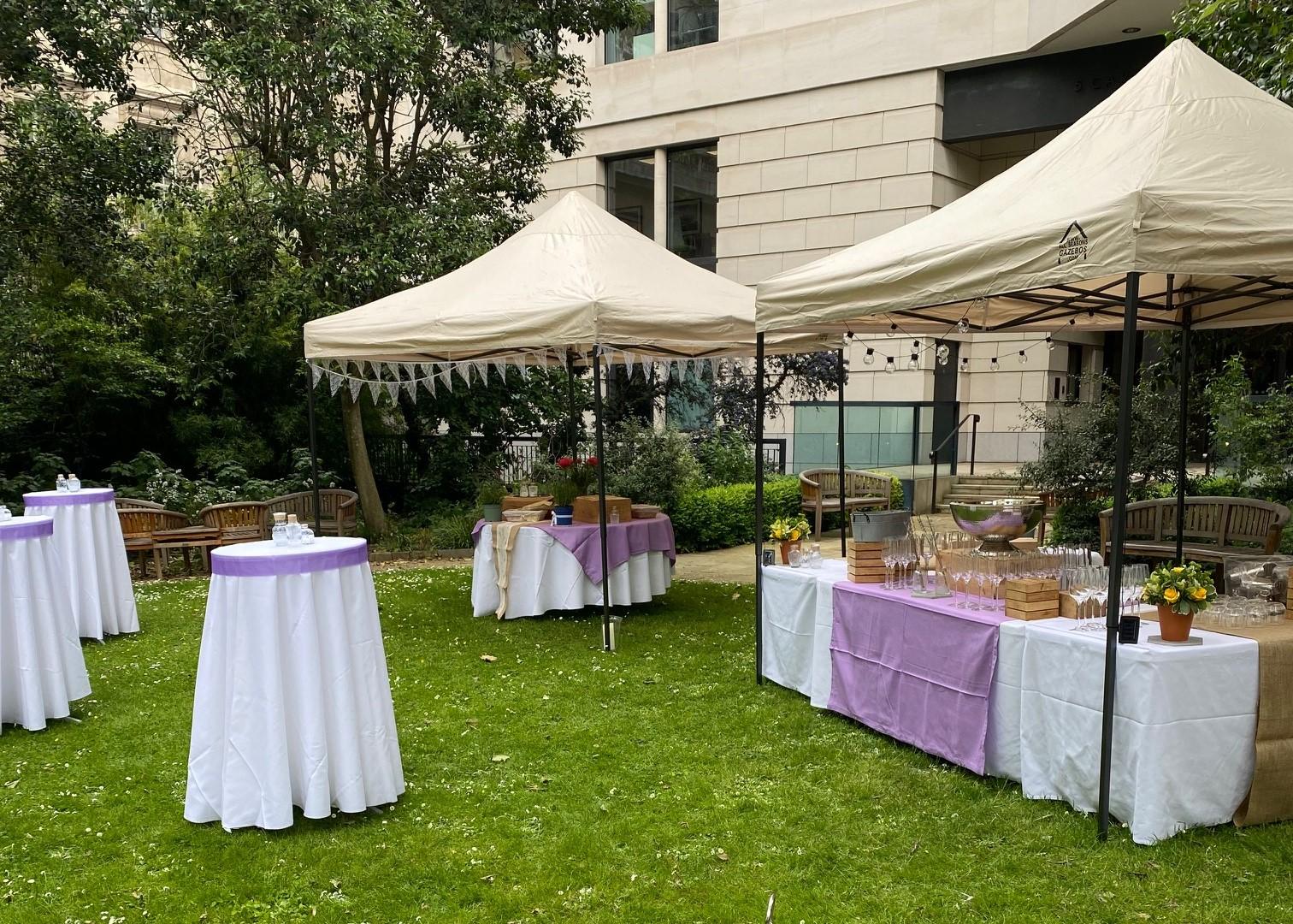 An outdoor event venue with cocktail tables covered in white linens and pop-up canopy tents at Prince Philip House.