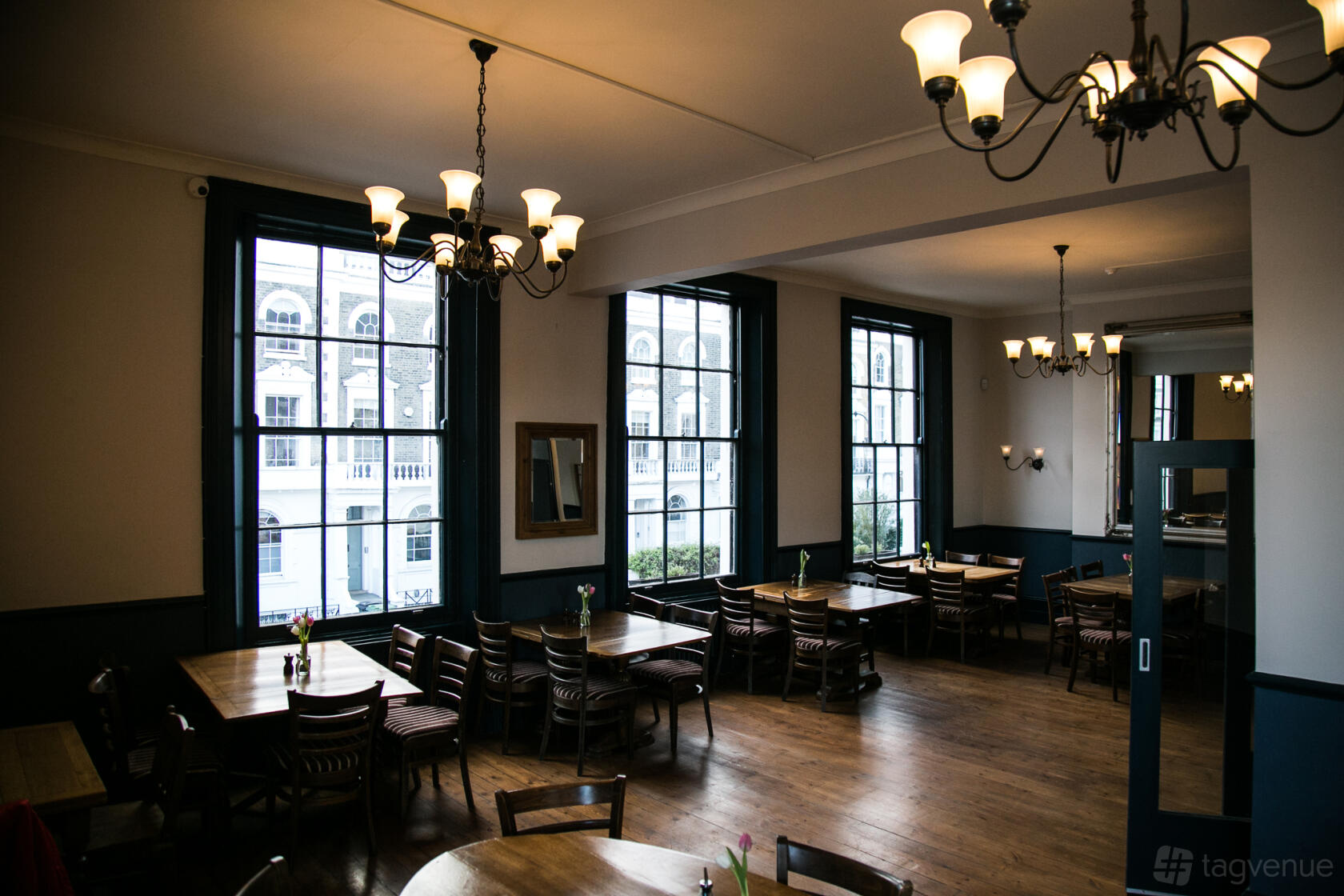 A function room with large windows, wooden floors, and multiple tables with chairs at The Lansdowne Pub & Dining Room.