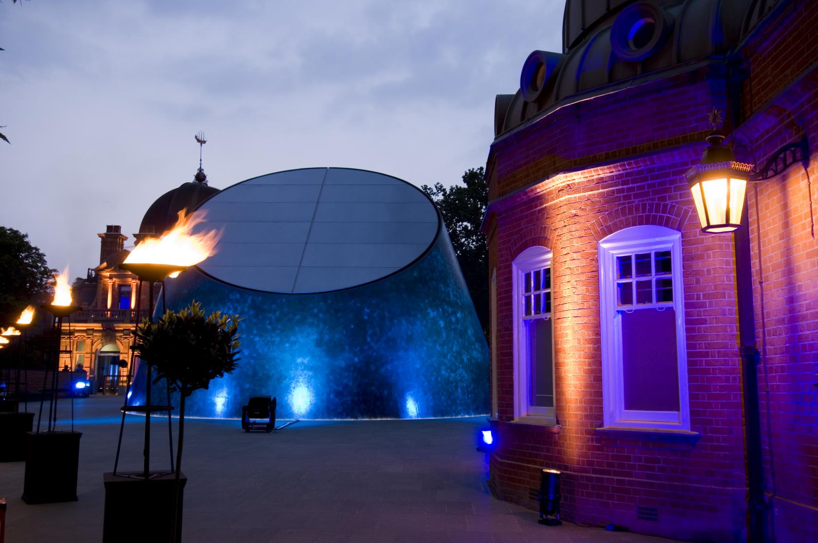 A museum exterior with a curved glass dome, brick walls, and dramatic evening lighting at The Peter Harrison Planetarium.