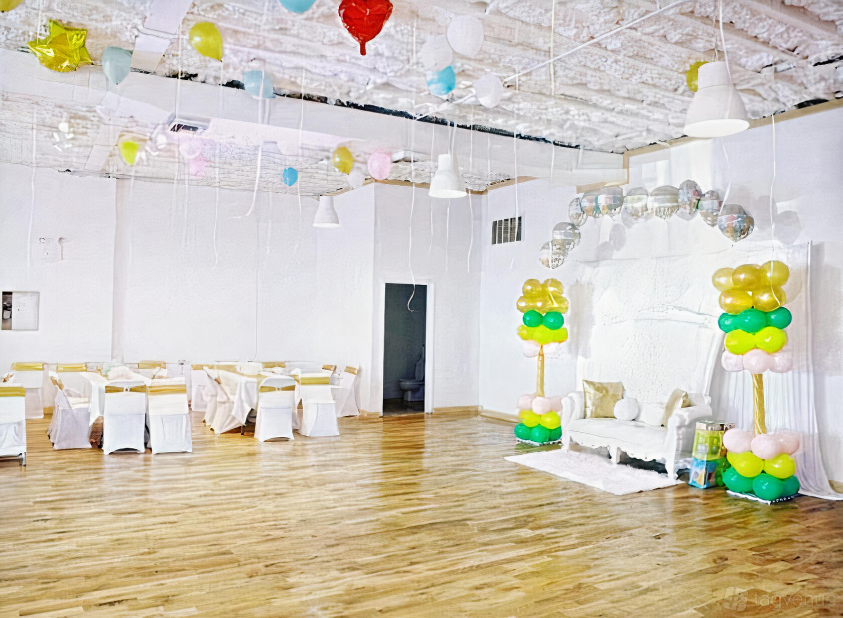 An event venue with polished wood floors, white walls, pastel balloons, and a decorated seating area at Elite Space.