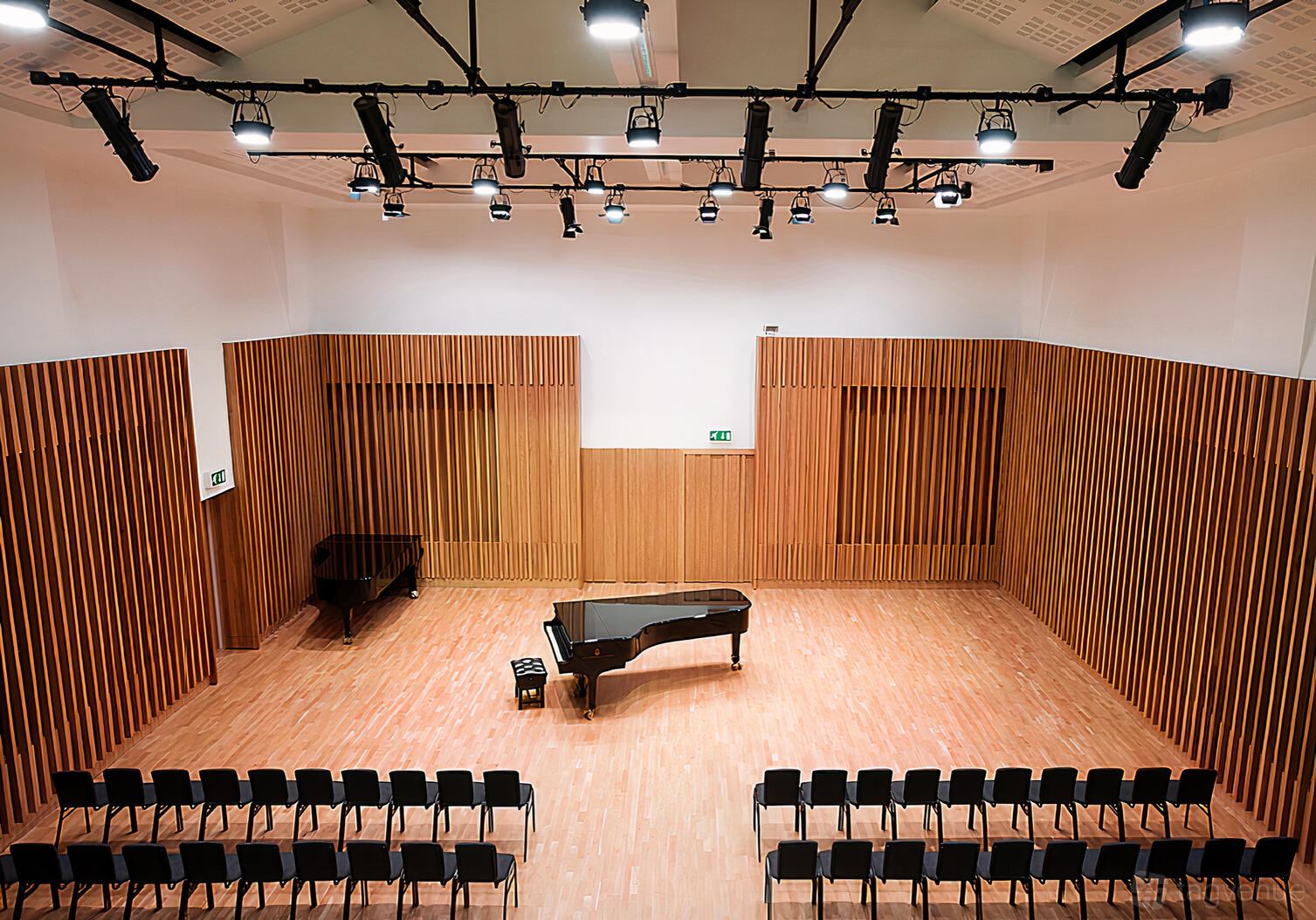 A concert hall with wood panel walls, two grand pianos, and rows of black chairs at Stoller Hall.