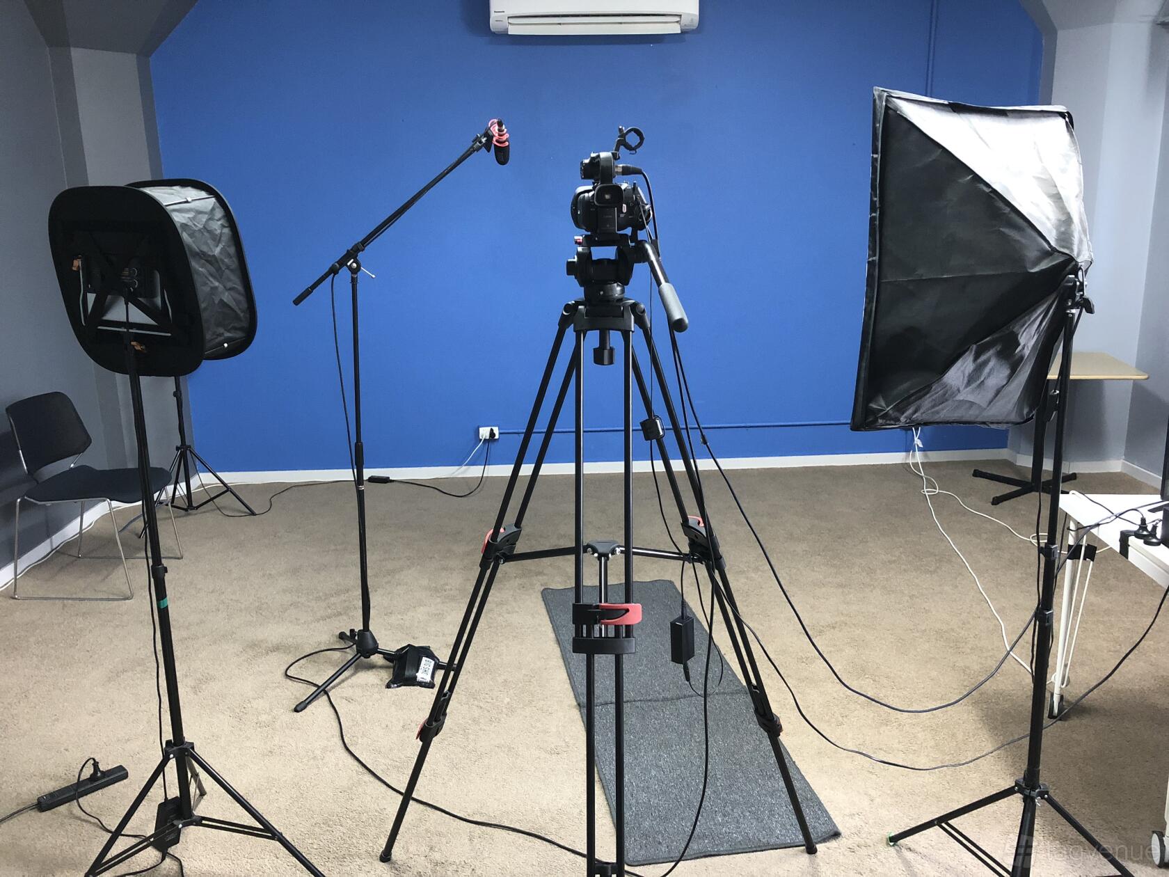 A photo studio with a blue accent wall, camera setup, softbox lighting, and microphones at TAFTA Studios.