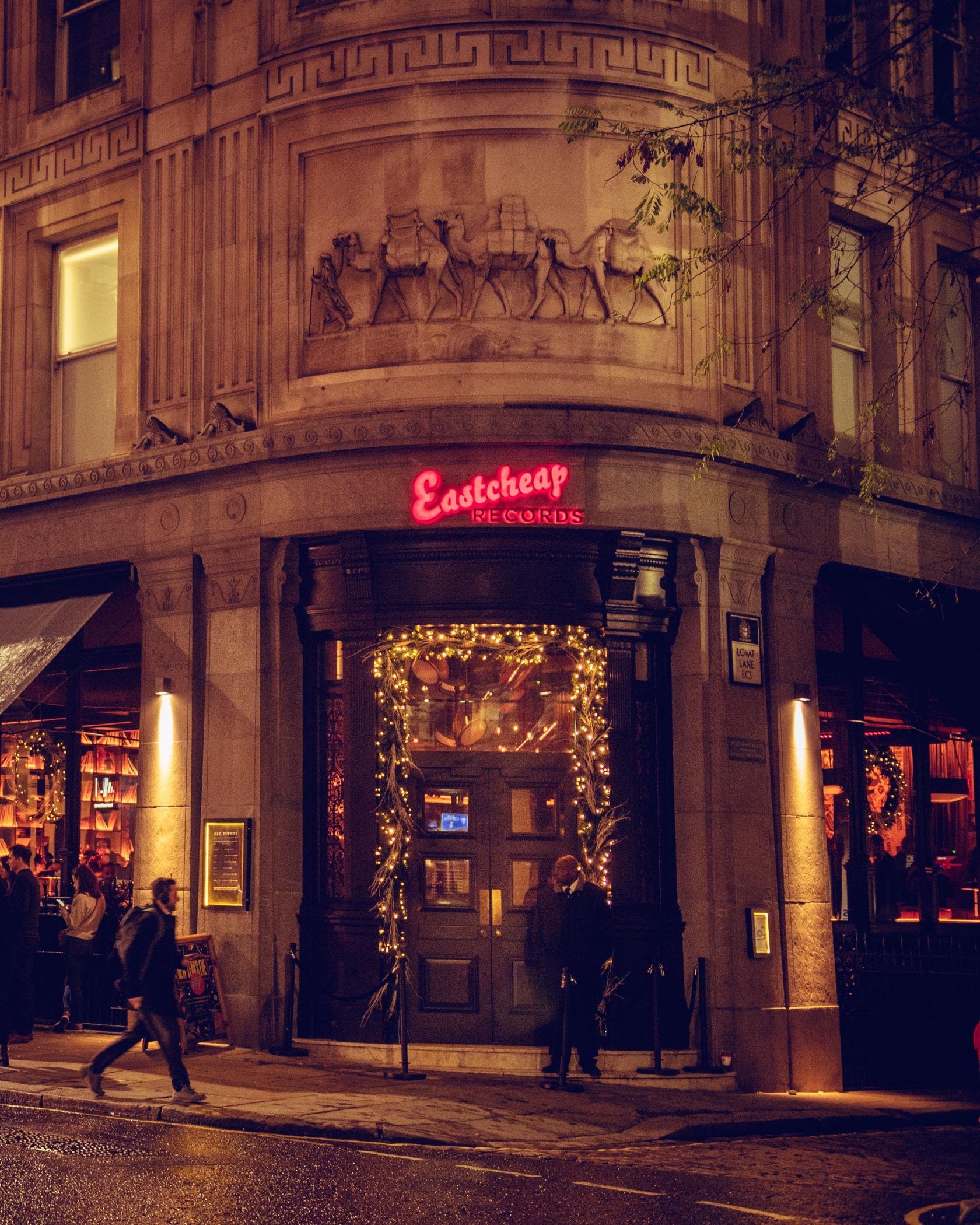 An event venue in a bar with a neon sign above the entrance and golden string lights at Eastcheap Records.