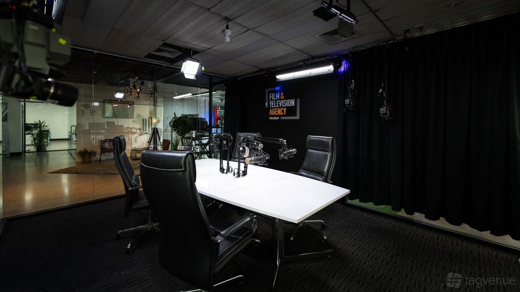 A recording studio with a white table, microphones, black office chairs, and hanging studio lights at WE FILM - Studio One.