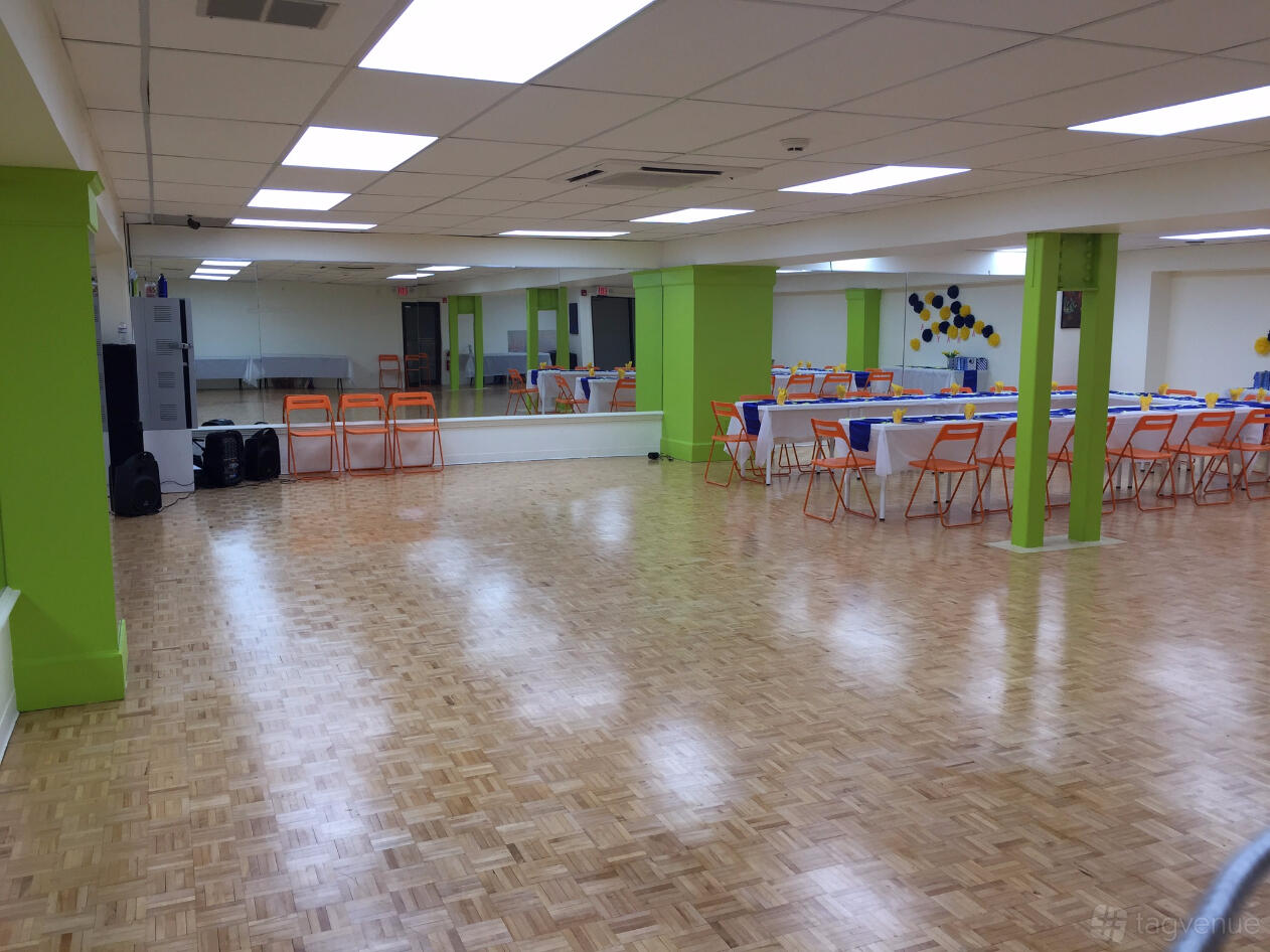 An event space with a polished parquet dance floor, mirrored wall, and folding chairs at Academy of Creative Arts.