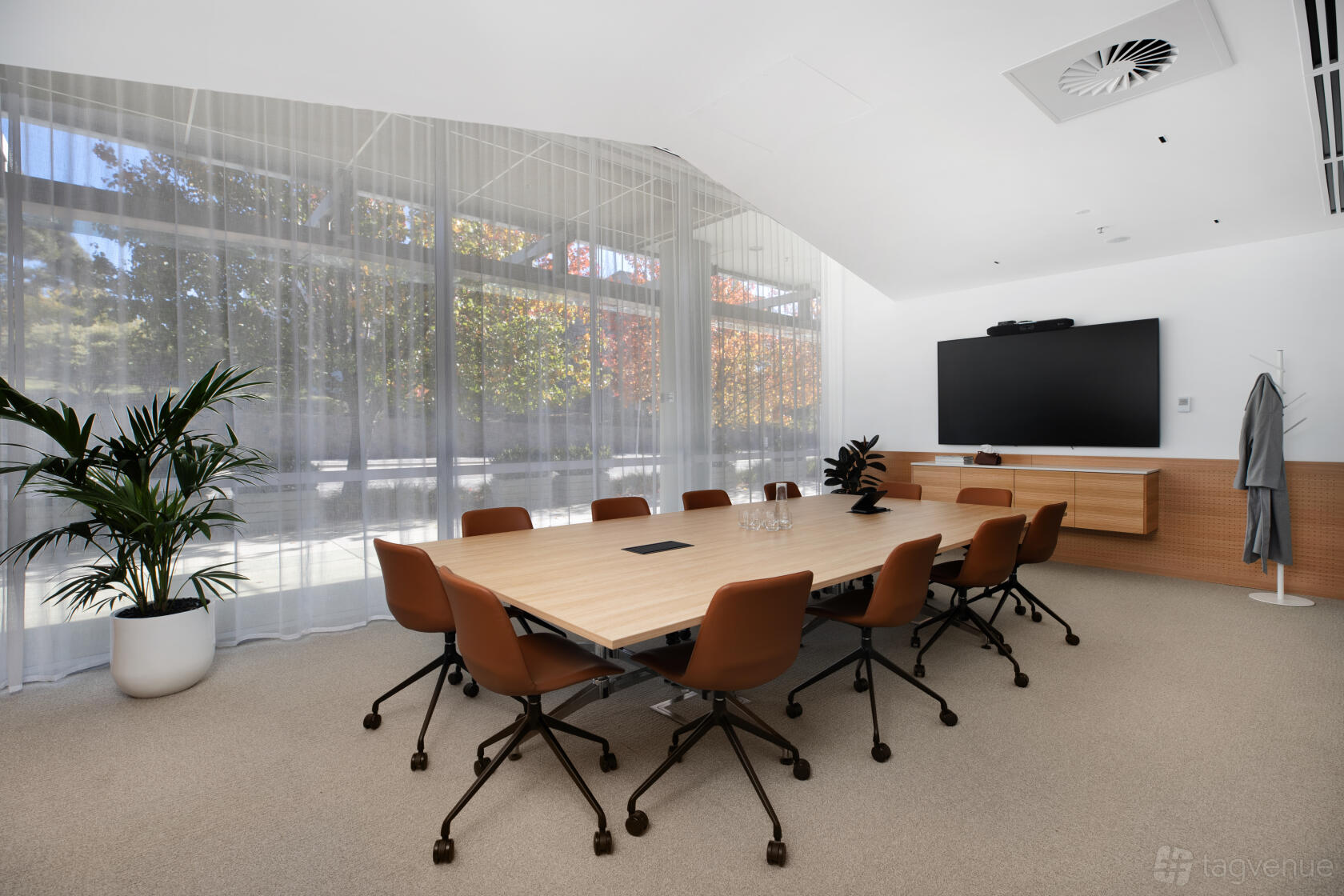 A meeting room with a large wooden table, brown chairs, floor-to-ceiling windows, and a wall-mounted screen at Flex by ISPT Pathway Place.
