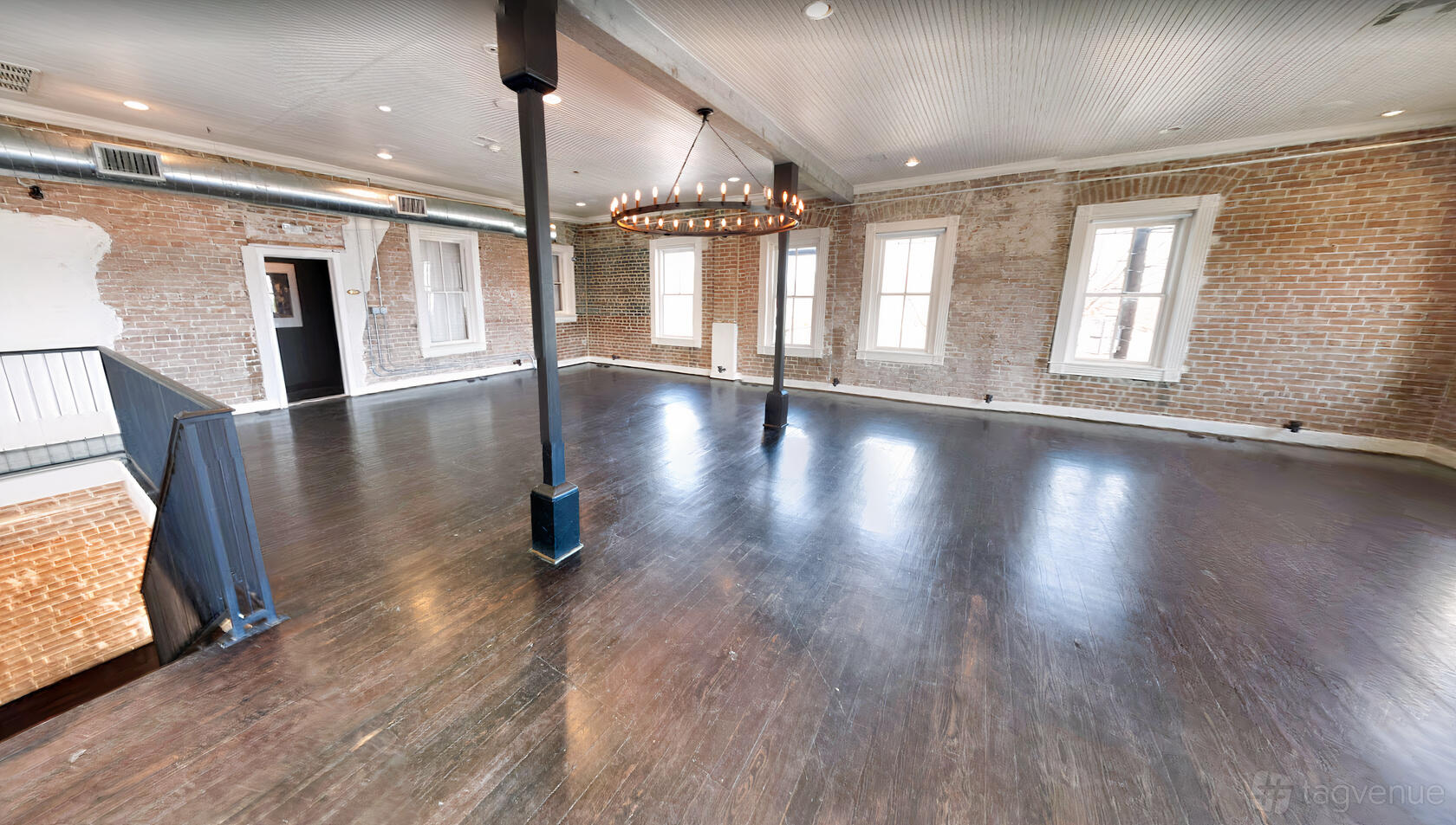 An event venue with exposed brick walls, large windows, dark wood floors, and a circular chandelier at Station 3.