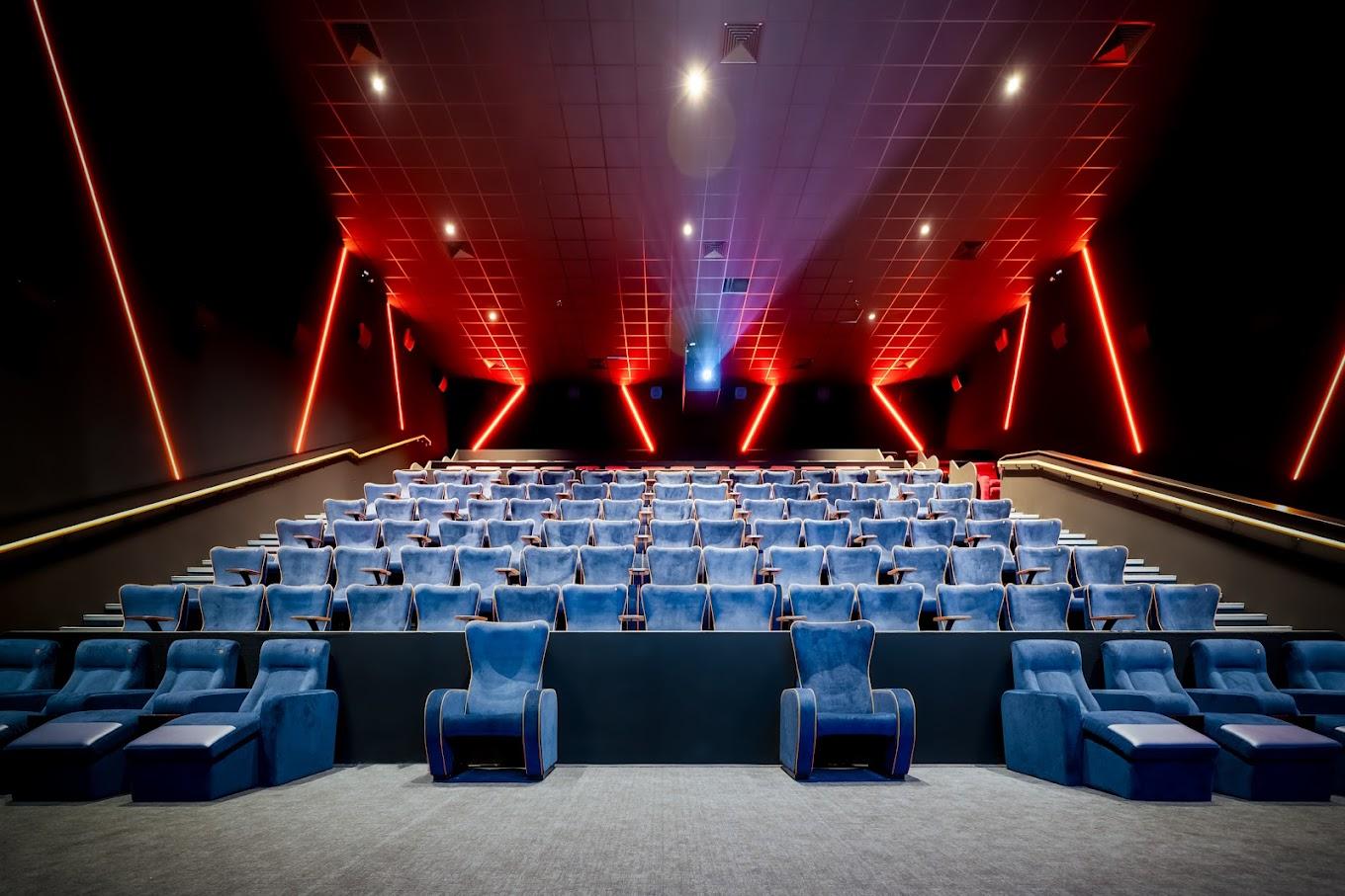 A cinema auditorium with tiered blue seating, plush recliners, and red accent lighting at The Light Redhill.