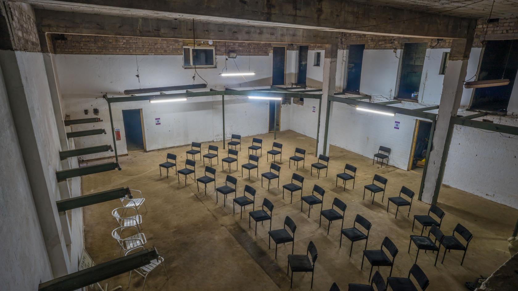 An event venue with rows of black chairs on a concrete floor and exposed brick walls at Barnton Bunker.
