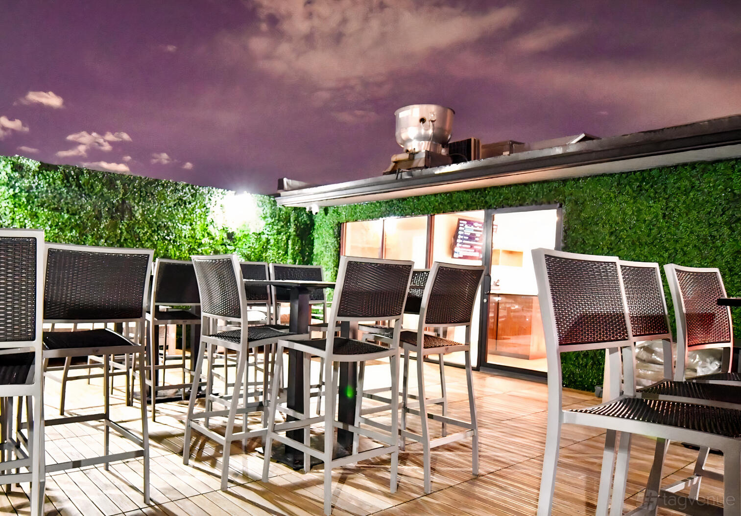 An outdoor restaurant patio with tall woven chairs, wooden decking, and green hedge walls at Air Restaurant.