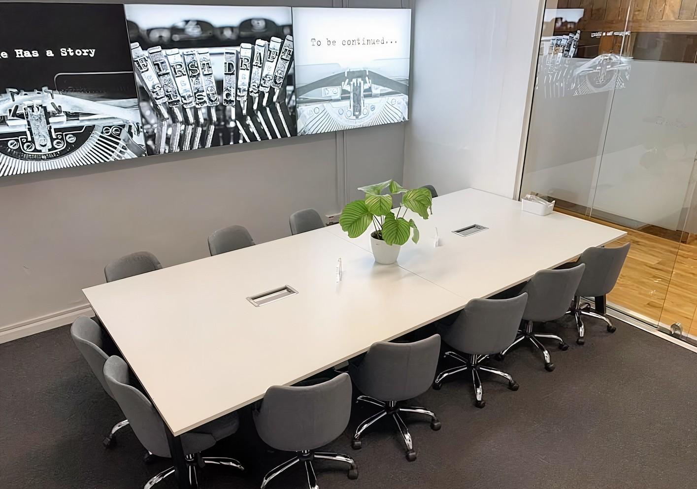 A meeting room with a white rectangular table, grey chairs, glass walls, and black-and-white artwork at Mill House Wooburn.