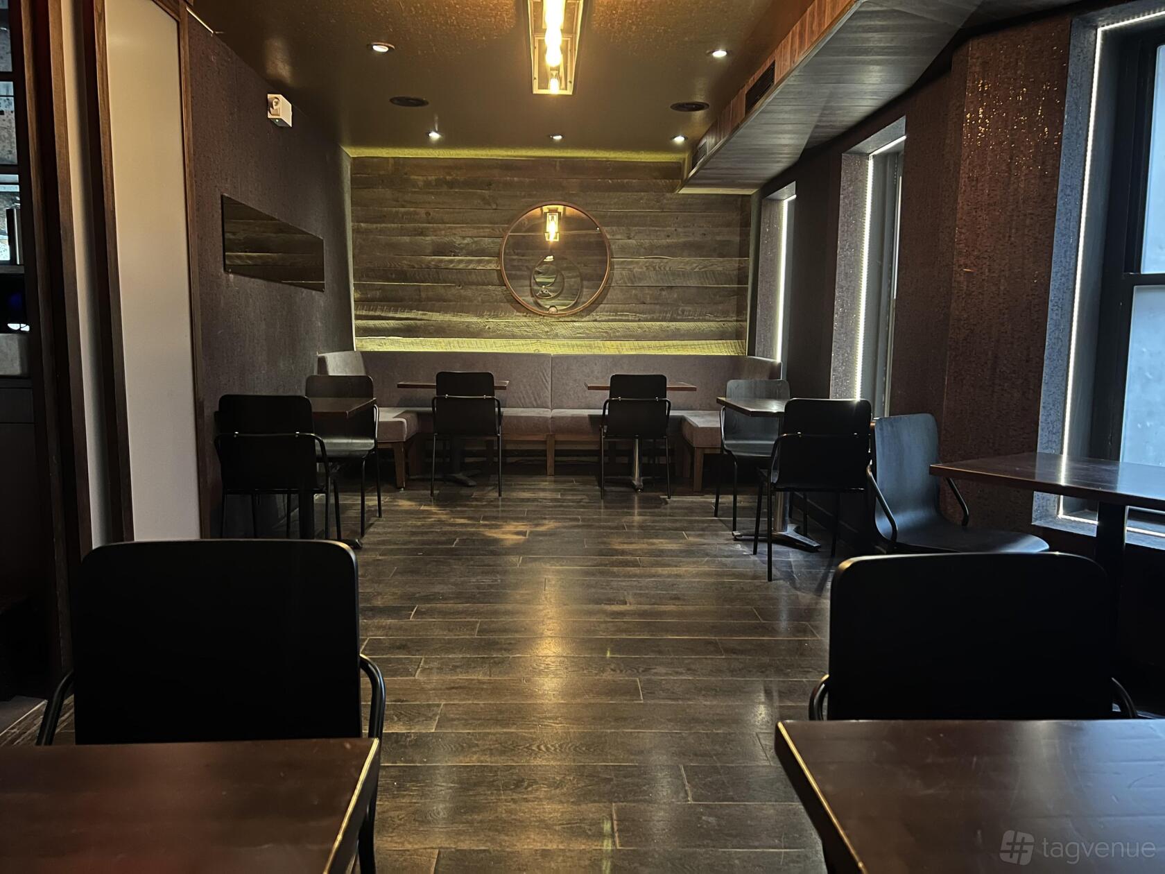 A dining room with dark wood floors, window seating, and a round mirror on a wood accent wall at Ama Raw Bar West Village.