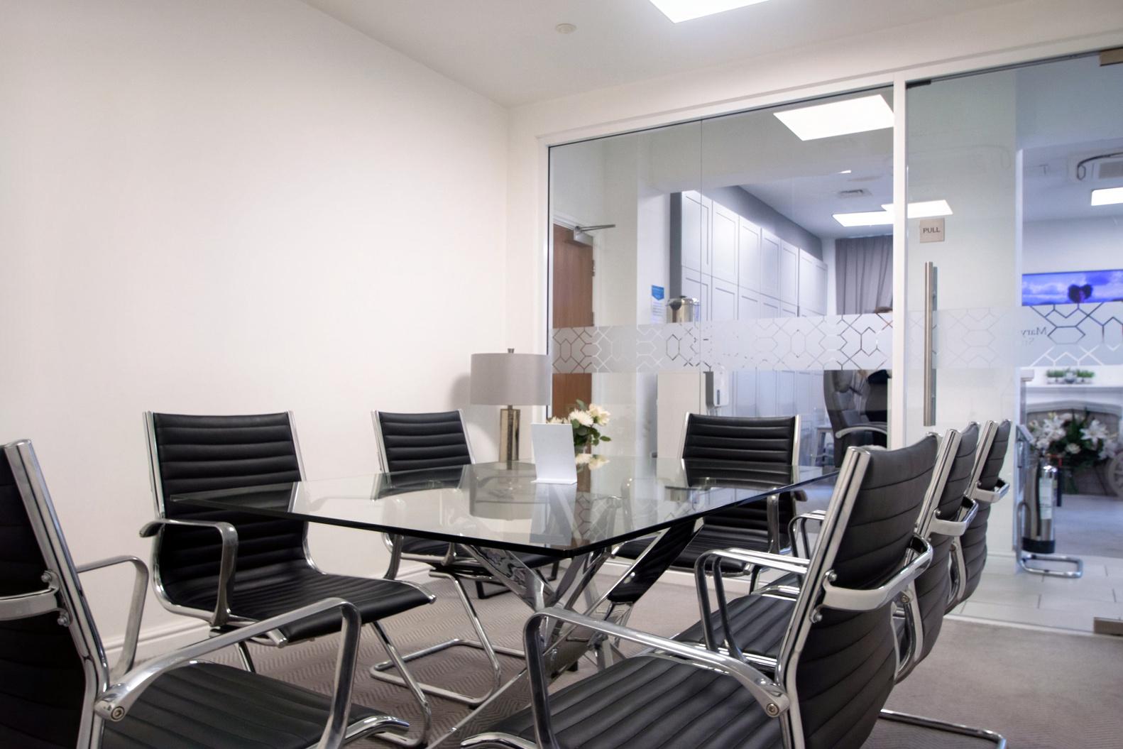 A meeting room with a glass table, black leather chairs, and frosted glass wall at Grosvenor House.