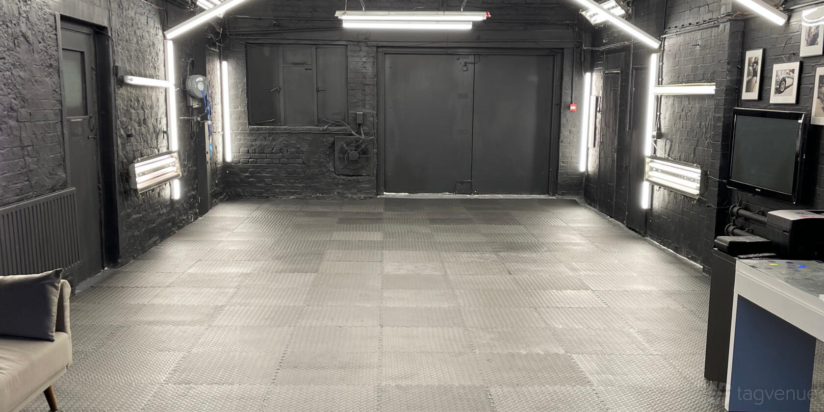 A photo studio with black painted brick walls, industrial lighting, and textured flooring at E.C. Car Detailing.