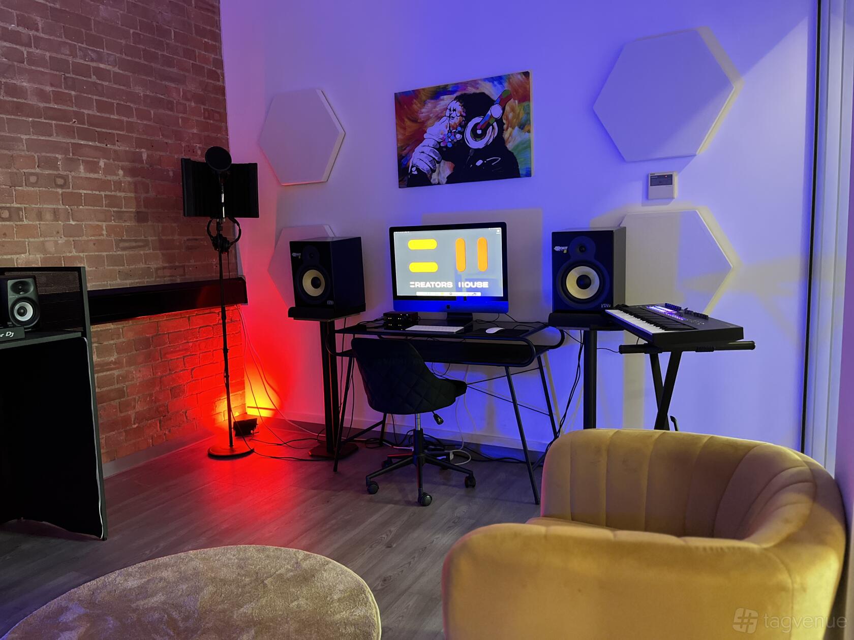 A music studio with exposed brick walls, a recording microphone, sound panels, and studio monitors at Creators House.