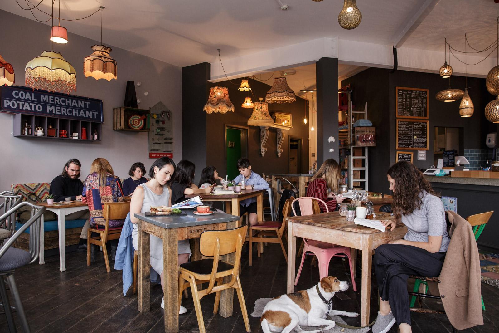 A cafe with eclectic pendant lighting, mismatched wooden tables, and wall art at Esquires Coffee Balham.