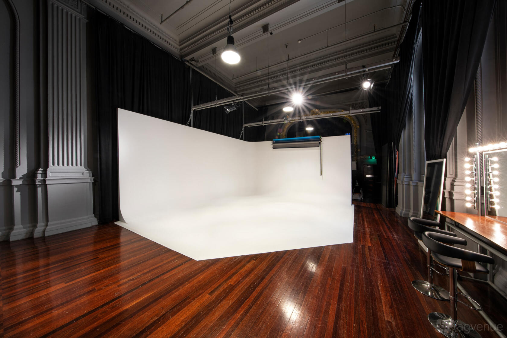 A photo studio with a white cyclorama wall, polished wood floors, and makeup station mirrors at Studio Commercial.